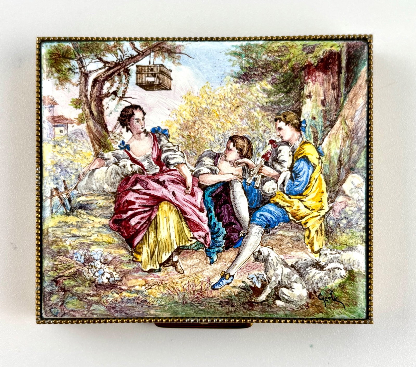Viennese 19th Century Enamel Compact with Pastoral Scene: Rectangular brass compact with an enameled lid depicting a vibrant pastoral scene featuring three figures in 18th century attire and surrounding naturalistic details, including a birdcage and dogs. Th