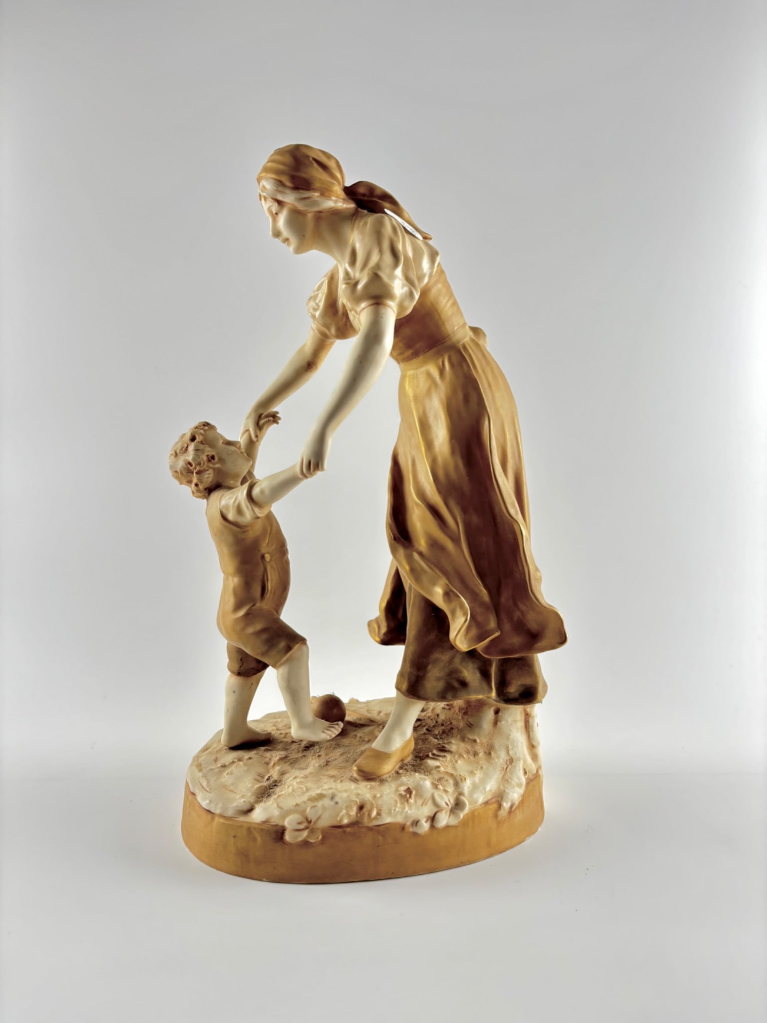 Royal Dux Bohemia Figural Porcelain Group, Model 1312: A Royal Dux Bohemia porcelain sculpture, model number 1312, depicting a mother in a flowing gown engaging with a young child. Crafted with hand-painted details and finished in soft beige and amber ton