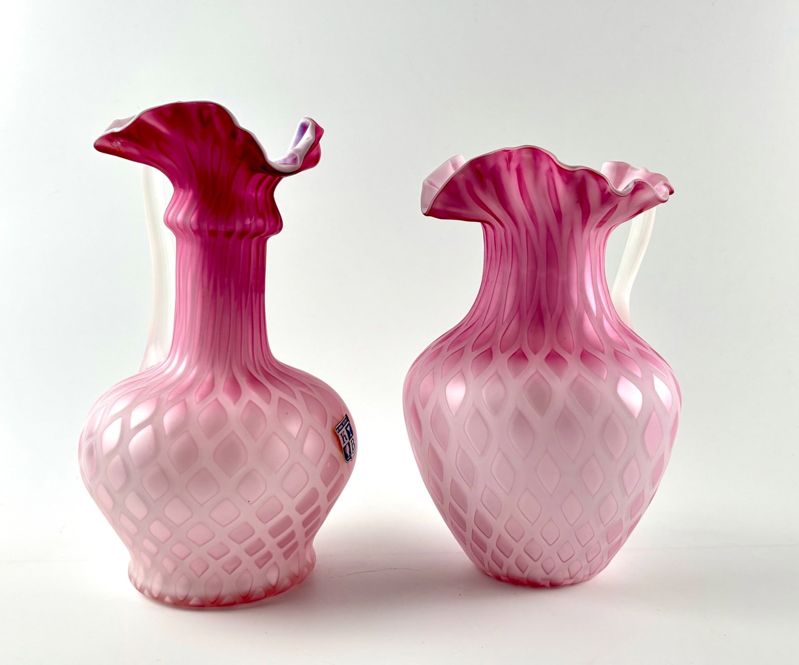 Murano Pink Satin Glass Ewers by KB with Ruffled Rims: Handmade Italian pink satin glass ewers by KYB, featuring a diamond-quilted pattern and twisted clear glass applied handles. Each ewer is adorned with a ruffled rim transitioning from deep pink to lig