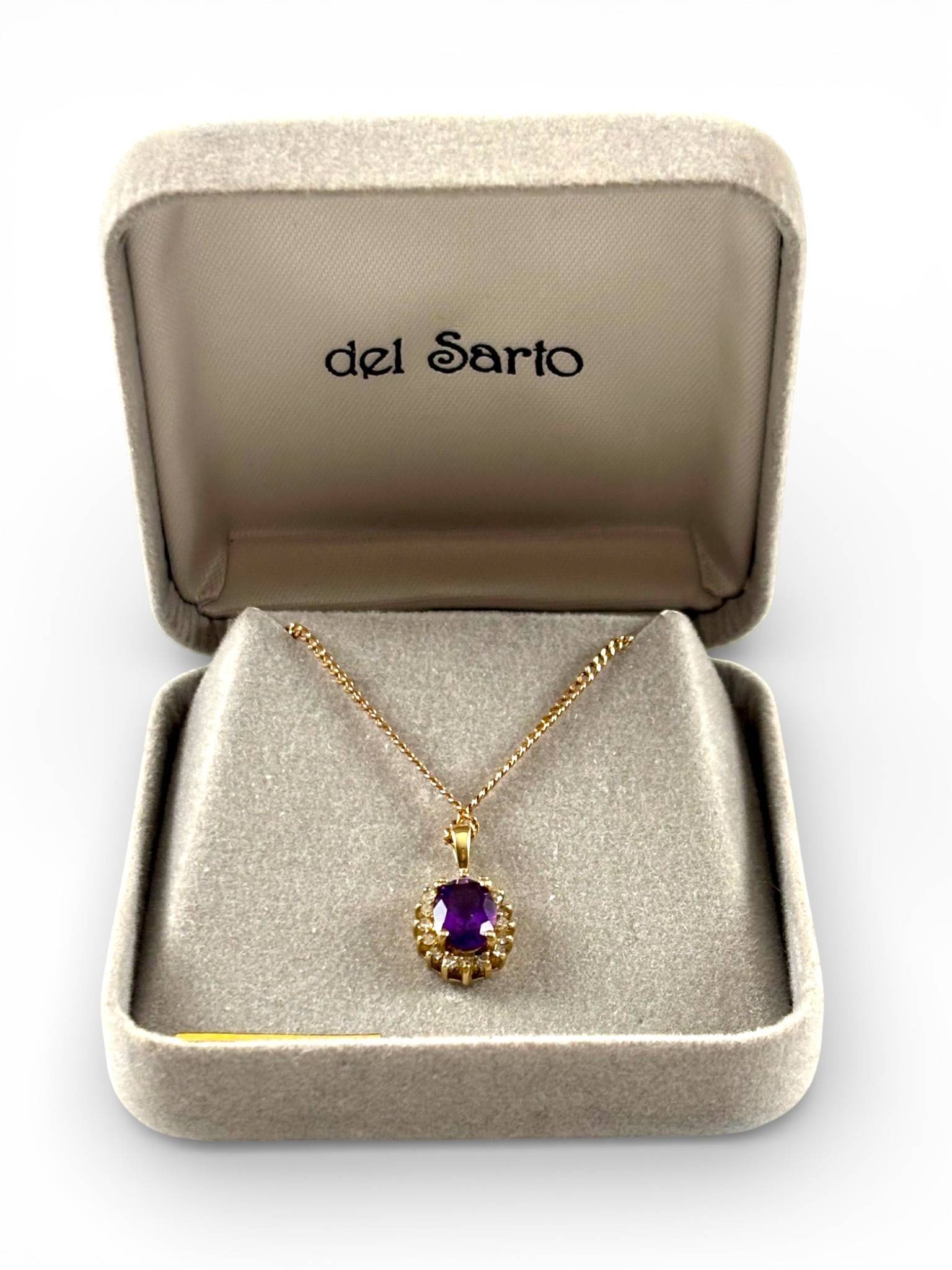 10K Gold Pendant Necklace with Amethyst and Diamond Accents: Gold pendant necklace featuring an oval cut amethyst surrounded by 16 small diamond accents set in 10K yellow gold. The pendant is suspended from an 18 inch chain with a spring ring clasp marked 10K.