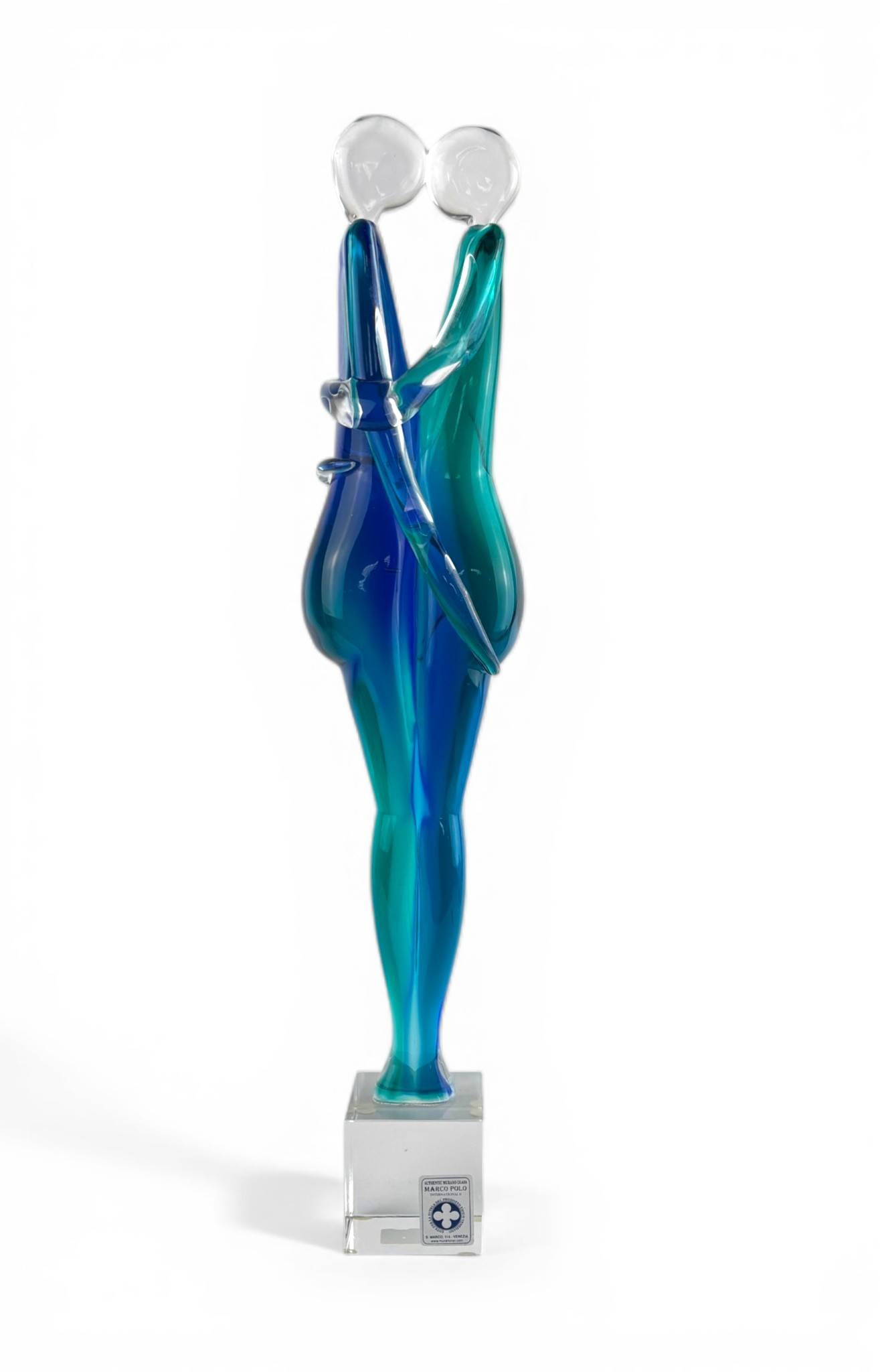 Murano Glass Lovers by Marco Polo: A Murano glass sculpture depicting an abstract embracing couple in translucent blue and green tones. Made by Marco Polo as indicated by the label on the clear rectangular base. The figurine stands on