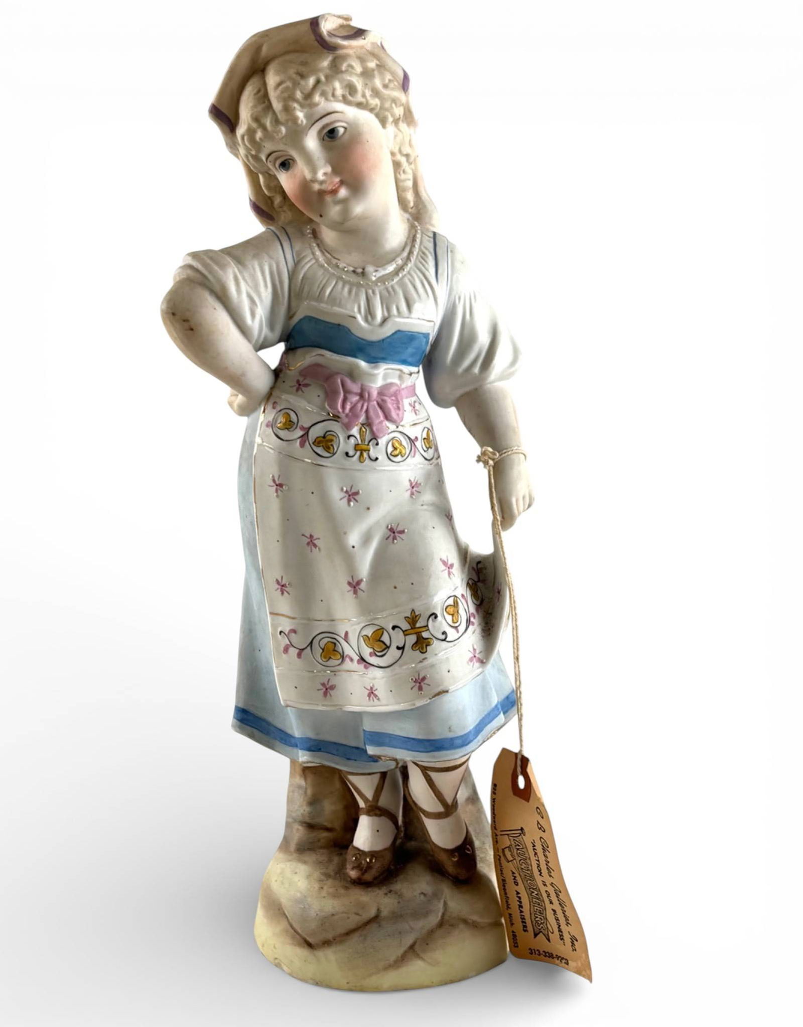 Germain Bisque Porcelain Figurine of a Young Girl: A bisque porcelain figurine attributed to Germain, depicting a young girl in a detailed hand painted dress and headscarf. The figure features intricate floral designs on the apron, pastel accents, and