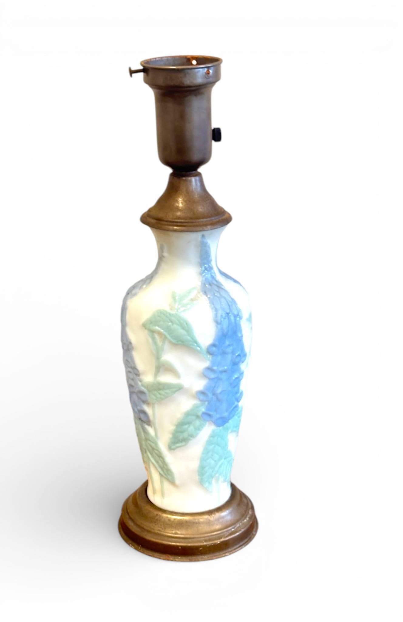 Phoenix Consolidated Glass Blue Flower Table Lamp Base: Phoenix Consolidated Glass lamp base featuring a textured blue flower and green leaf motif on an off white ground. The base and upper section are constructed of brass toned metal. Some wear is
