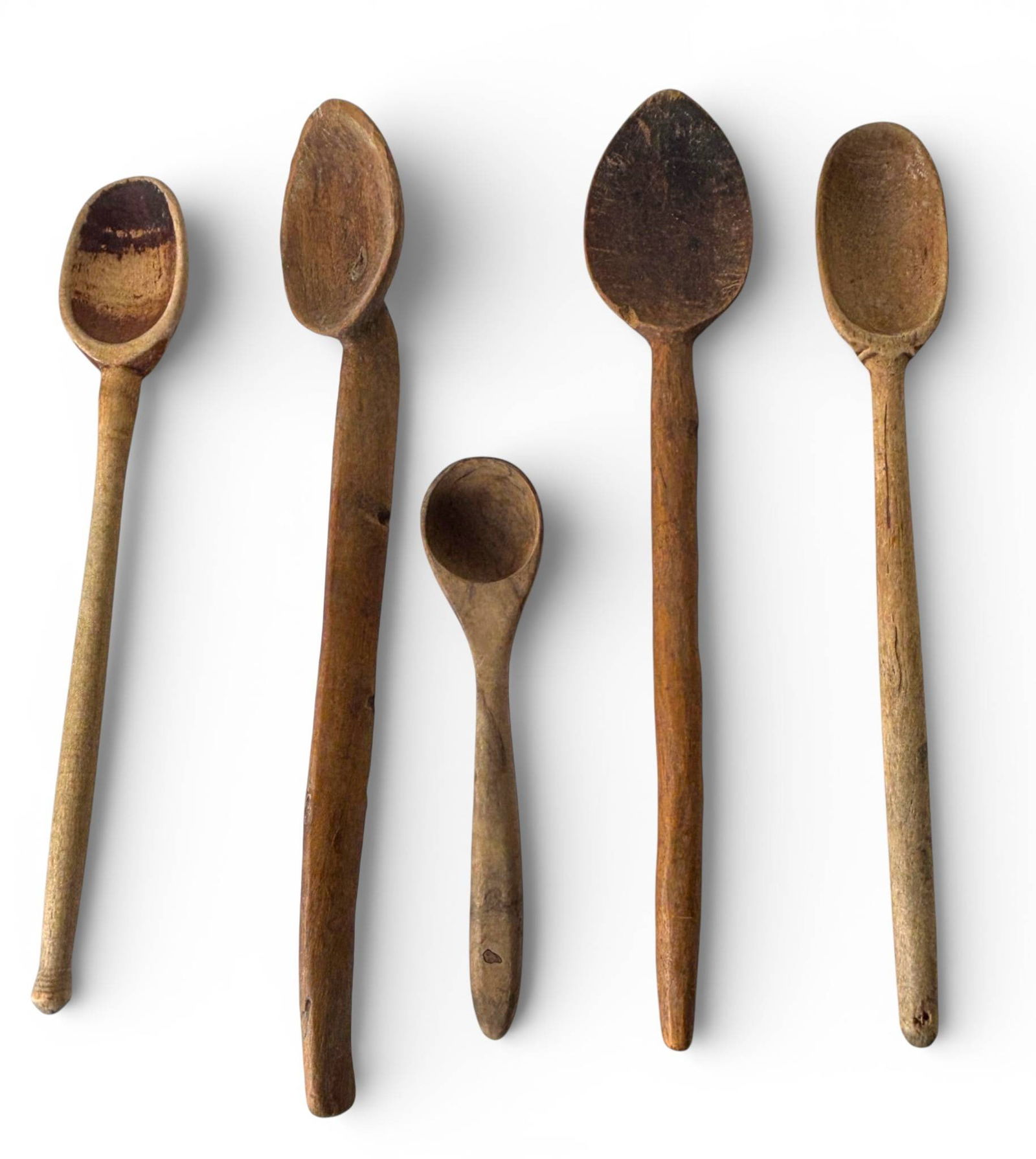 Primitive Hand Carved Wooden Spoons: Five hand carved wooden spoons exhibiting a rustic, primitive style. Each spoon varies in size and shape, showcasing craftsmanship with irregular features and natural wear consistent with the material