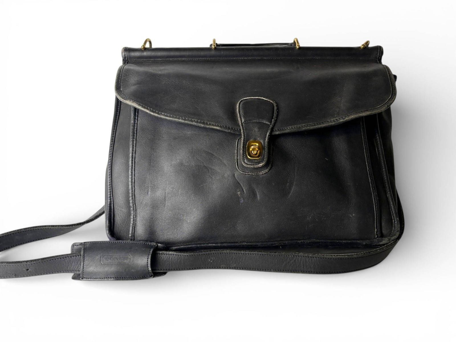 Vintage Coach Black Leather Messenger Bag with Brass Hardware: Vintage black leather Coach messenger bag featuring a front flap with a turn lock brass closure. The bag includes a single top handle and an adjustable shoulder strap with stitched padding. Brass hard