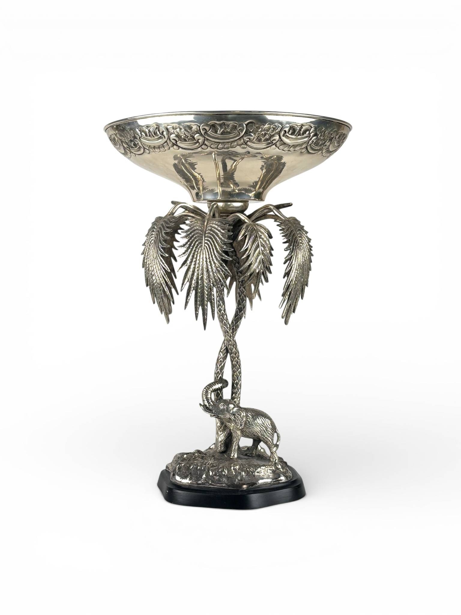 Victorian Exotica Silver Plate Elephant Tazza with Palm Design: Silver plated tazza featuring an intricate design with a shallow bowl resting on a stem designed as palm leaves and a tree trunk, which is supported by a base depicting an elephant in relief on natura