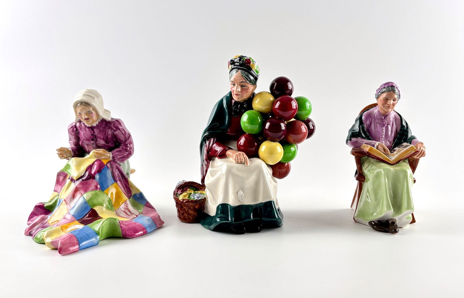 Three Royal Doulton Porcelain Figurines Featuring The Old Balloon Seller,Patchwork, and The Family: Three hand painted Royal Doulton porcelain figurines. Includes The Old Balloon Seller H.N. 1315, Patchwork H.N. 2351, and The Family Album H.N. 2321. Each figurine features intricate detailing and vib