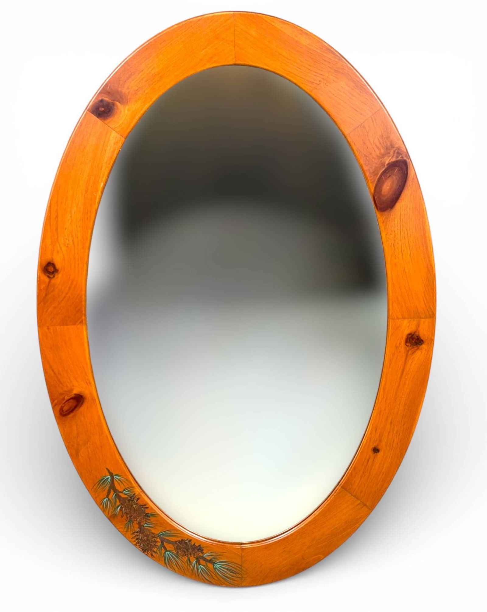 Oval Wood Framed Mirror with Carved Pine Cone Motif: An oval mirror with a polished wood frame featuring natural wood grain and a carved pine cone and pine needle design on the lower section. The back includes a wire for easy wall mounting. Frame shows
