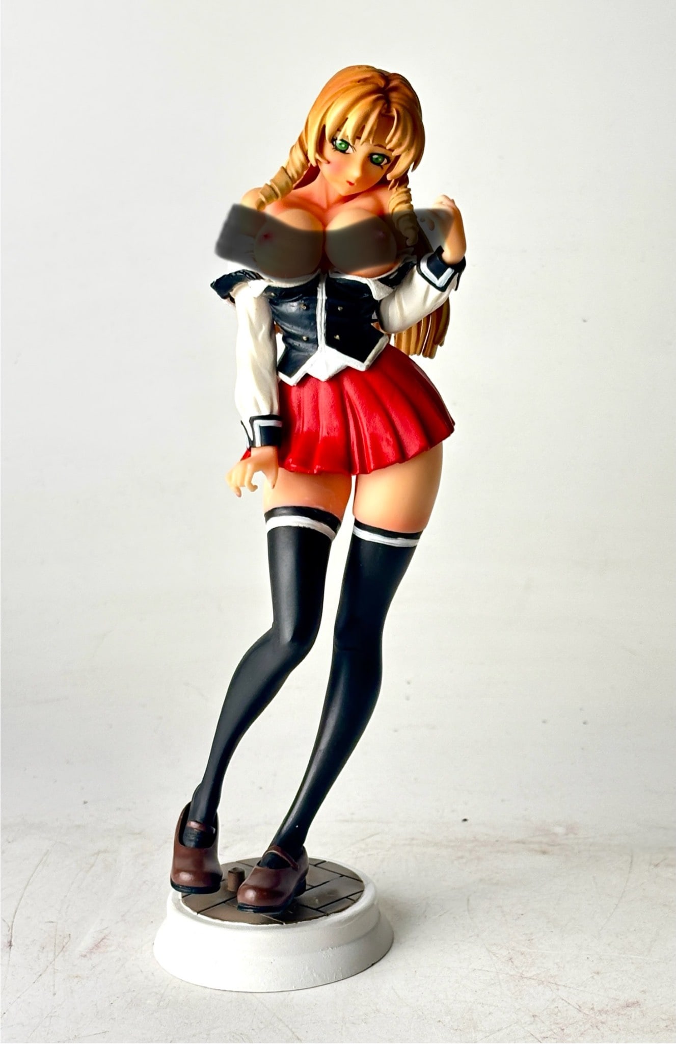 Hentai Inspired Anime Figure with Blonde Hair: A hentai inspired anime figurine featuring a female character with detailed blonde hair styled in braids. The character is dressed in a black and white top with a red pleated skirt, thigh high stockin
