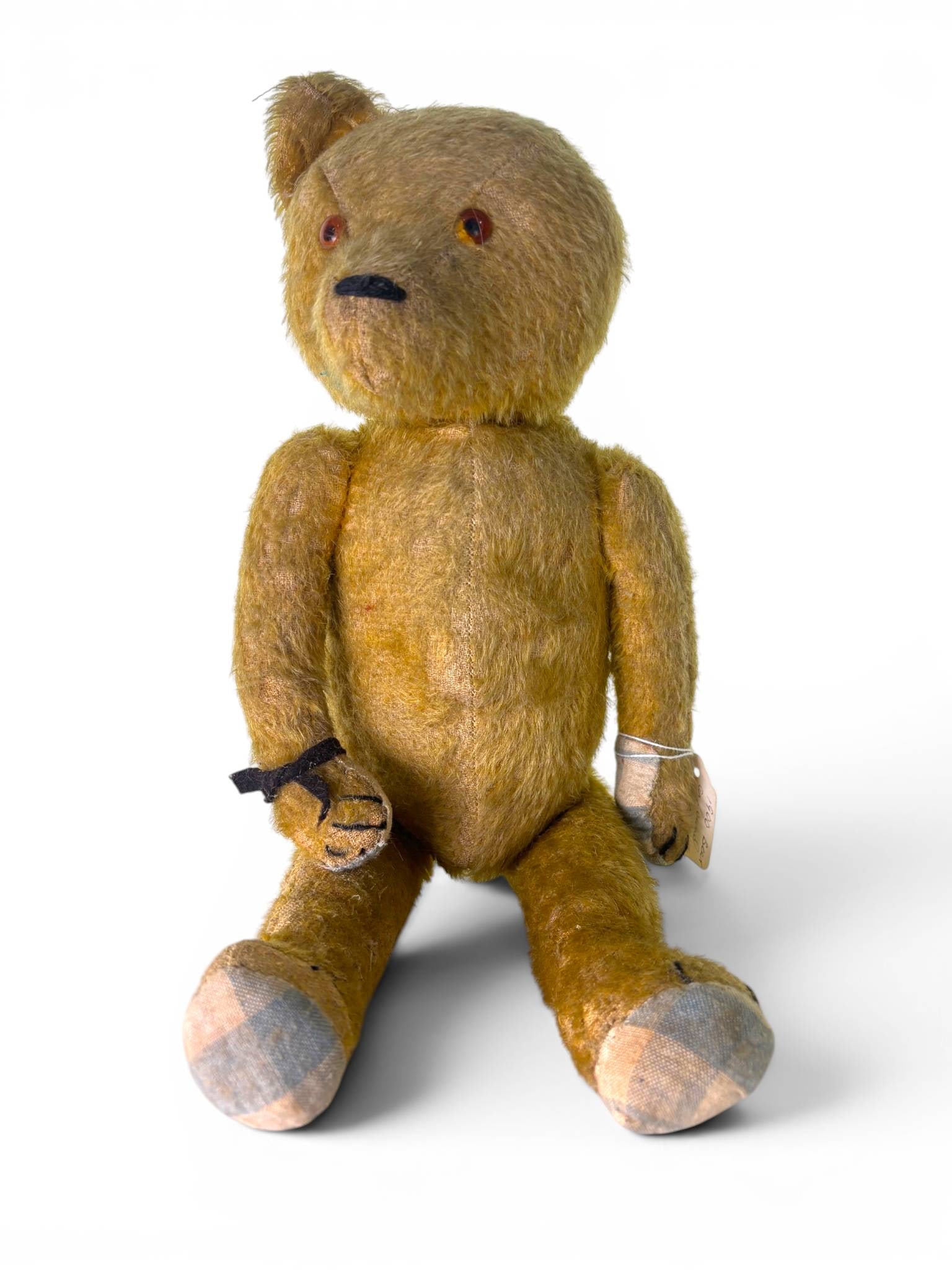 Early Mohair Straw Filled Jointed Teddy Bear 1900: Early jointed teddy bear made from golden mohair with straw filling. Features include shoe button eyes, a hand-stitched nose and mouth, and repaired fabric on the paw pads. Overall wear consistent