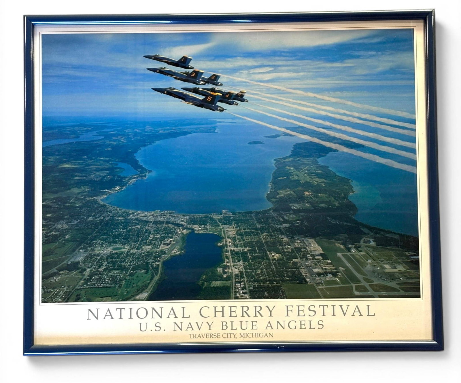 National Cherry Festival U.S. Navy Blue Angels Poster: A framed poster featuring an aerial view of Traverse City, Michigan, showcasing the U.S. Navy Blue Angels in synchronized flight during the National Cherry Festival. The image highlights the city’s