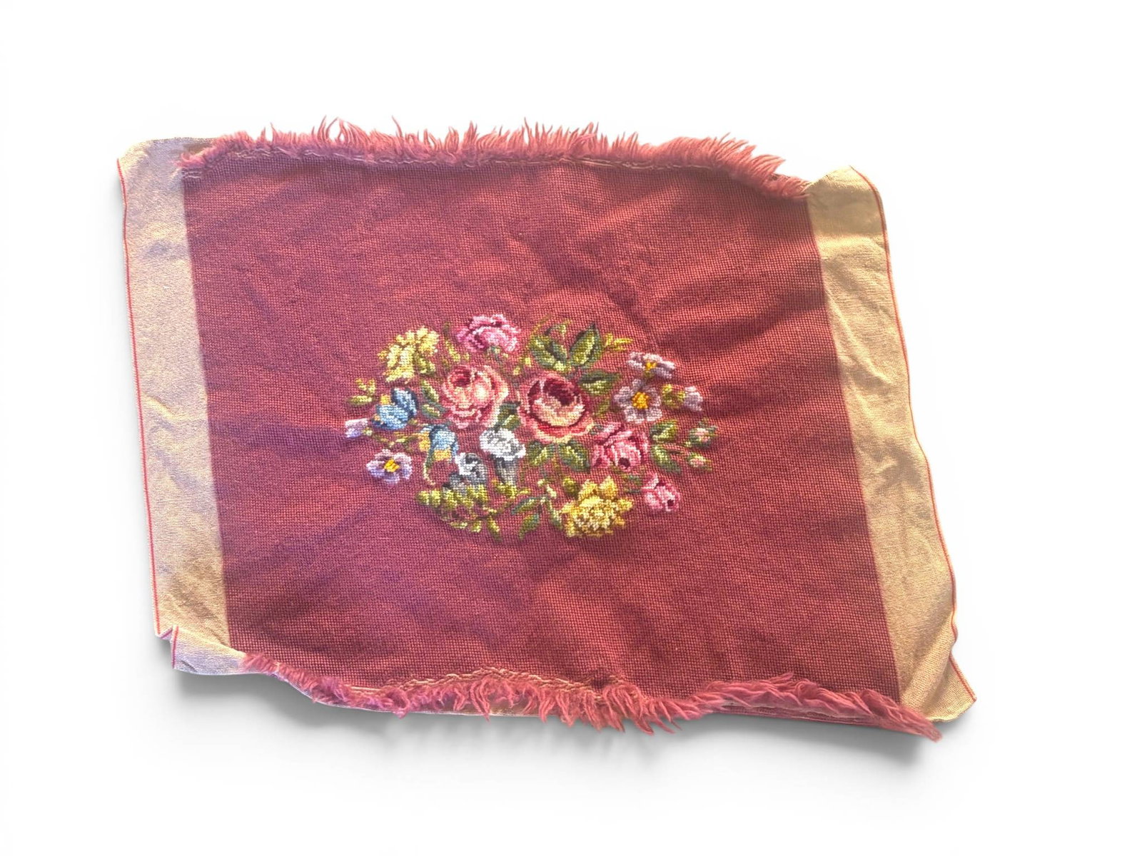 Needlepoint Textile Panel with Floral Motif: Rectangular textile panel featuring a floral embroidery design in multicolored threads on a red woven background. Gold toned borders frame the design, and the edges are frayed. Embroidery depicts rose