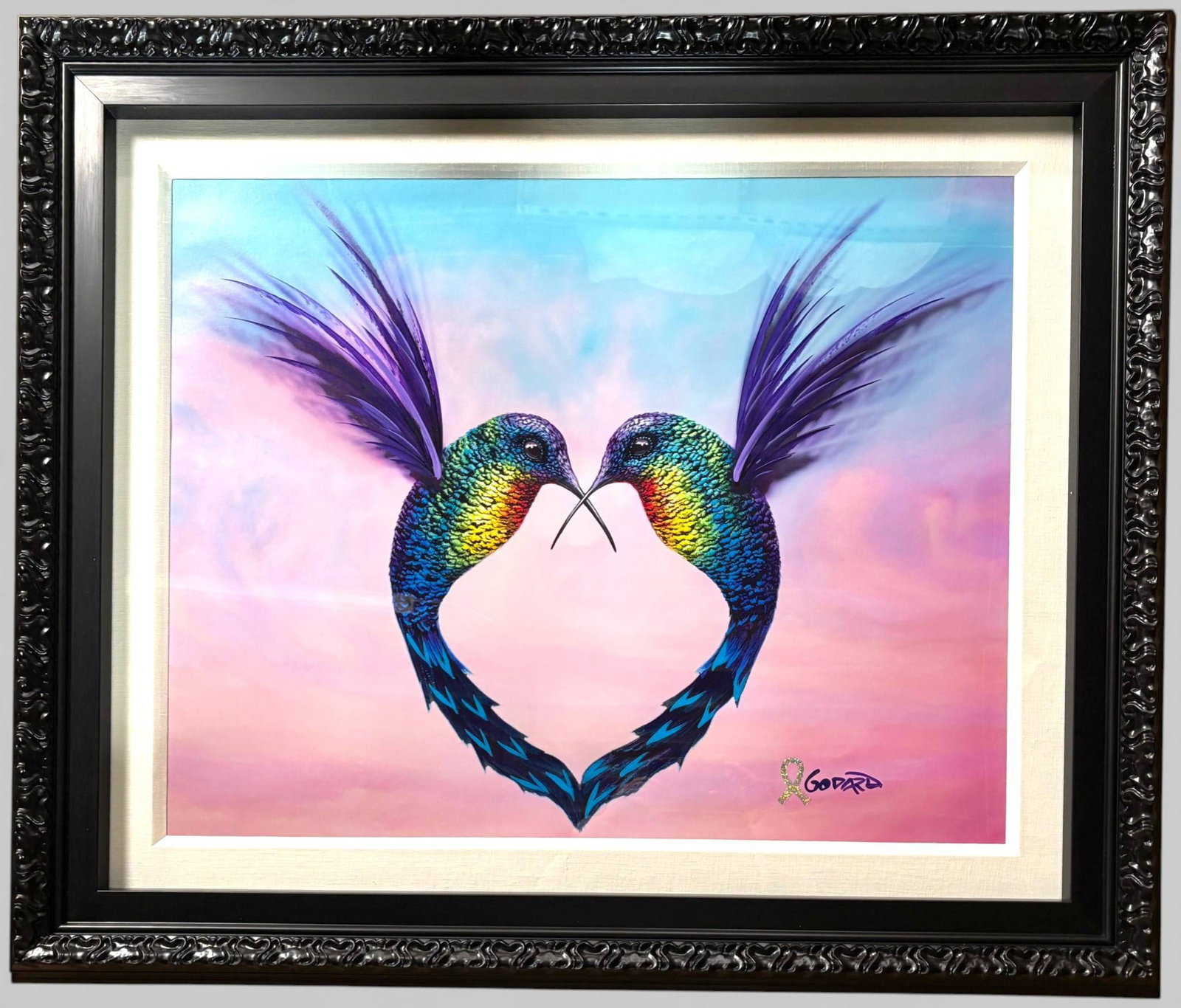 Framed Michael Godard Wings of Hope Mixed Media Artwork: Framed Michael Godard mixed media artwork titled Wings of Hope,depicting two vibrantly colored hummingbirds forming a heart shape with their bodies and wings against a pastel sky background. Features 