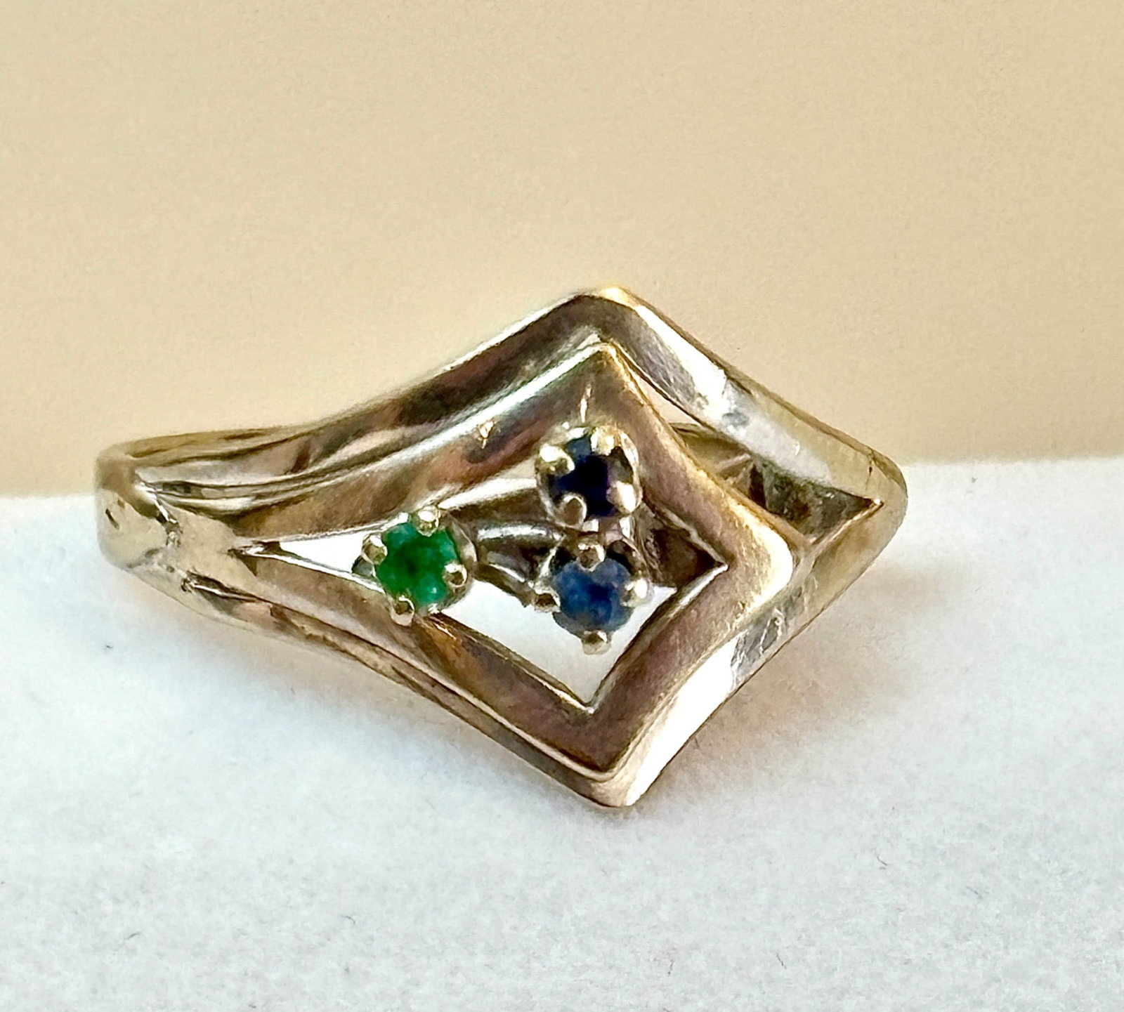 14K White Gold Ring with Openwork Design: 14K gold ring featuring a unique geometric openwork design. The piece is adorned with one green gemstone and two blue gemstones, all set in prongs within the central open section. The band tapers slig