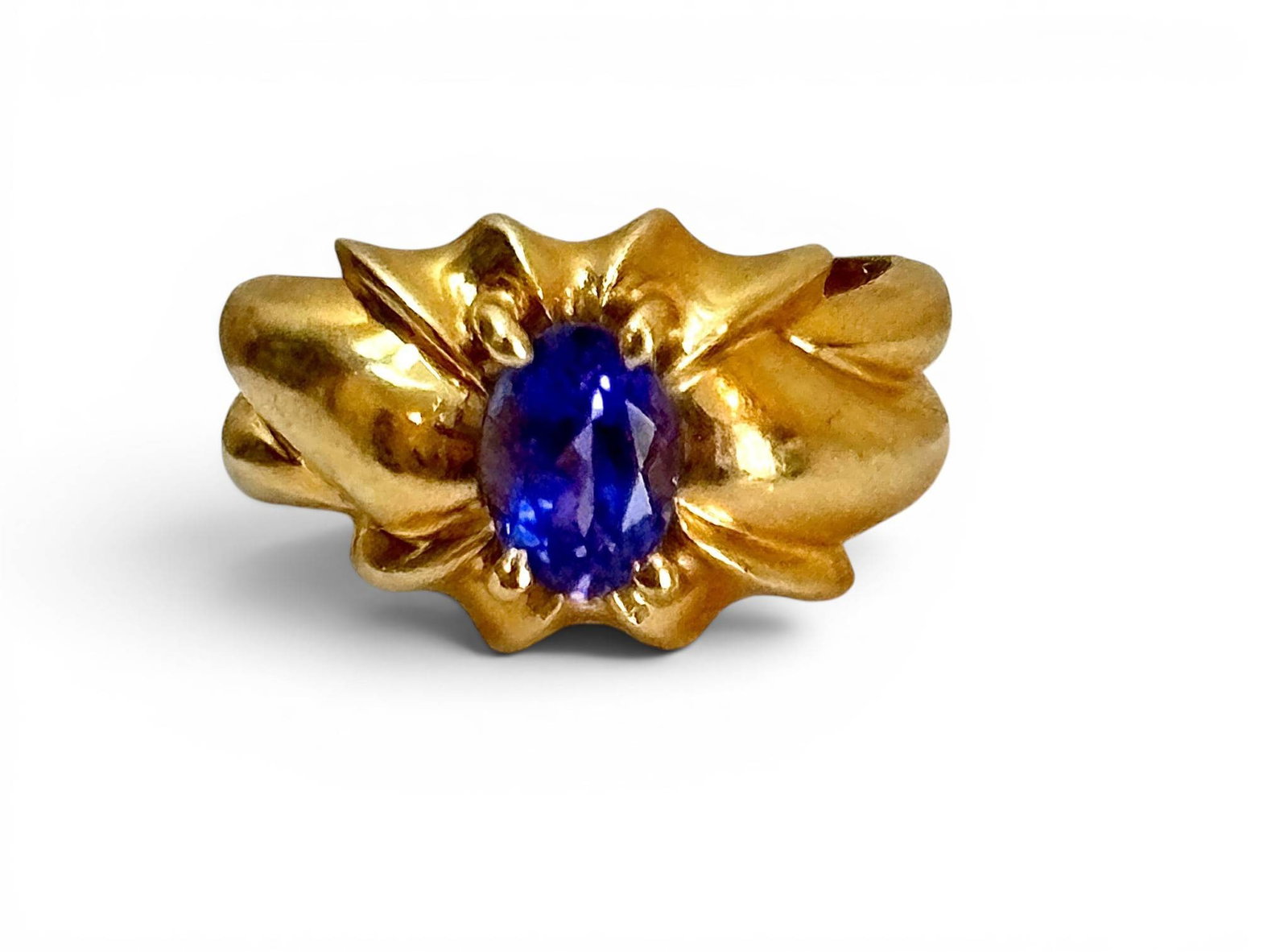 14K Gold Ring with Tanzanite Stone: 14K gold ring featuring an oval-cut faceted tanzanite stone in a prong setting. The band showcases a sculptural design with flowing, textured details that complement the stone. The inner shank is stam