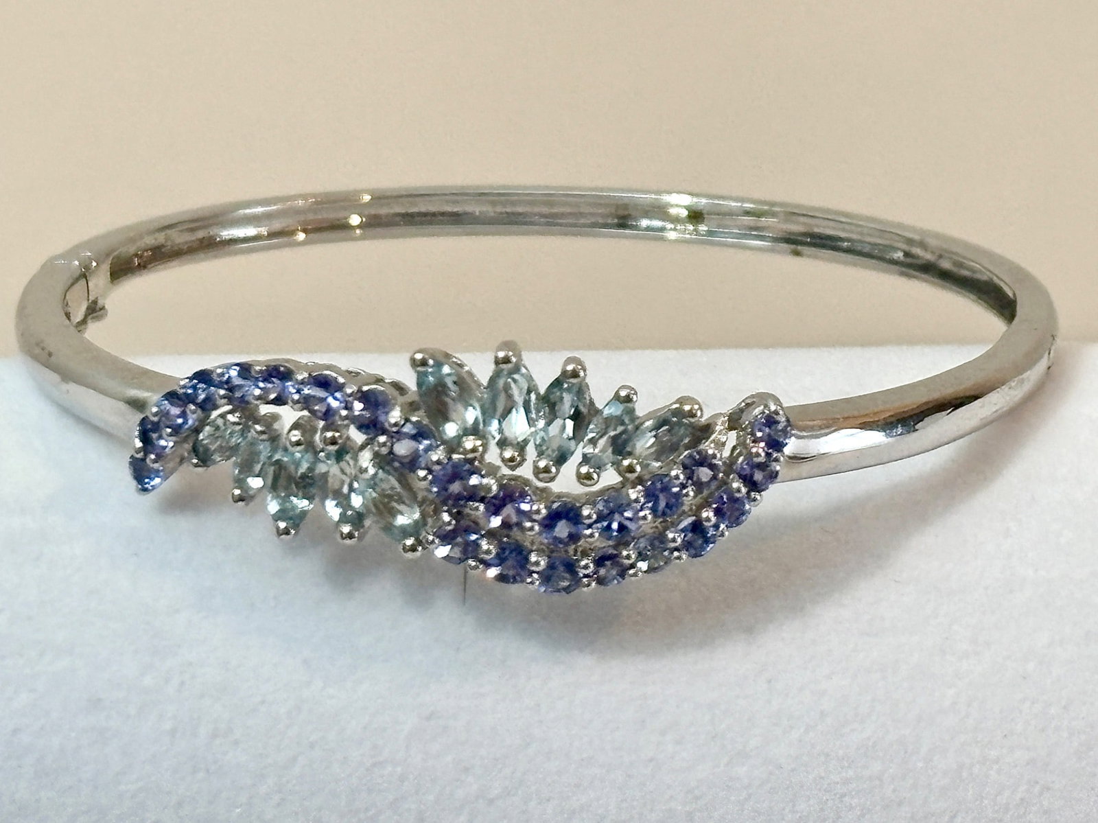 Sterling Silver Bangle with Tanzanite and Blue Topaz: A sterling silver bangle featuring marquise cut blue topaz and round cut tanzanite stones in a swirling design. The bracelet is crafted from 925 sterling silver, as marked on the interior. The hinged 