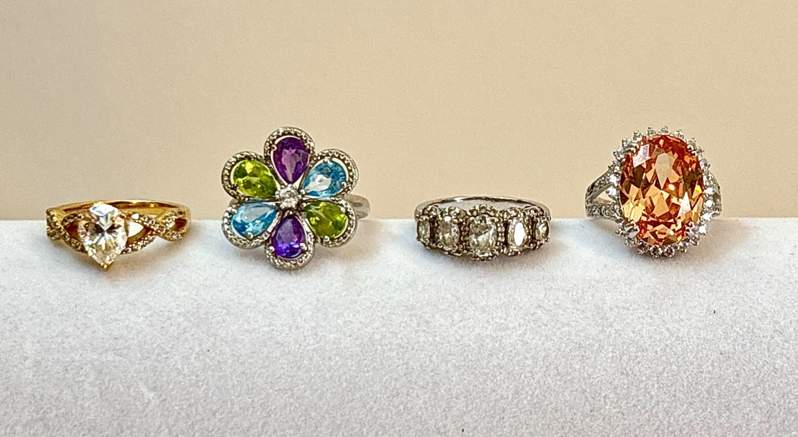 Four Sterling Silver Cocktail Rings: Four sterling silver cocktail rings, each with unique designs. Includes: a multicolored floral ring with gemstone petals, a large oval-cut orange gemstone ring framed with smaller white stones, a yell