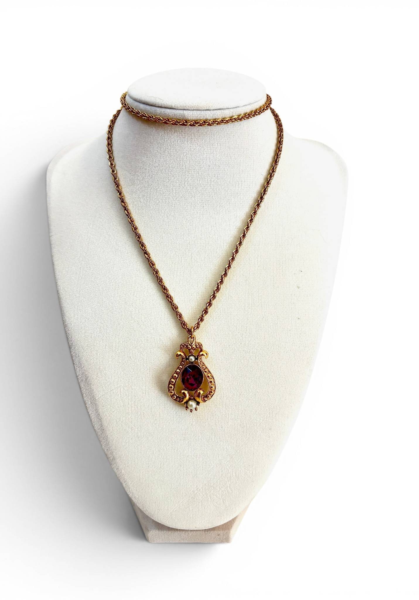 Avon Pendant Necklace: Gold-tone necklace by Avon featuring a decorative pendant with filigree design. The pendant showcases a central oval-cut faux amethyst stone accented by faux pearls. The pendant is attached to a twist