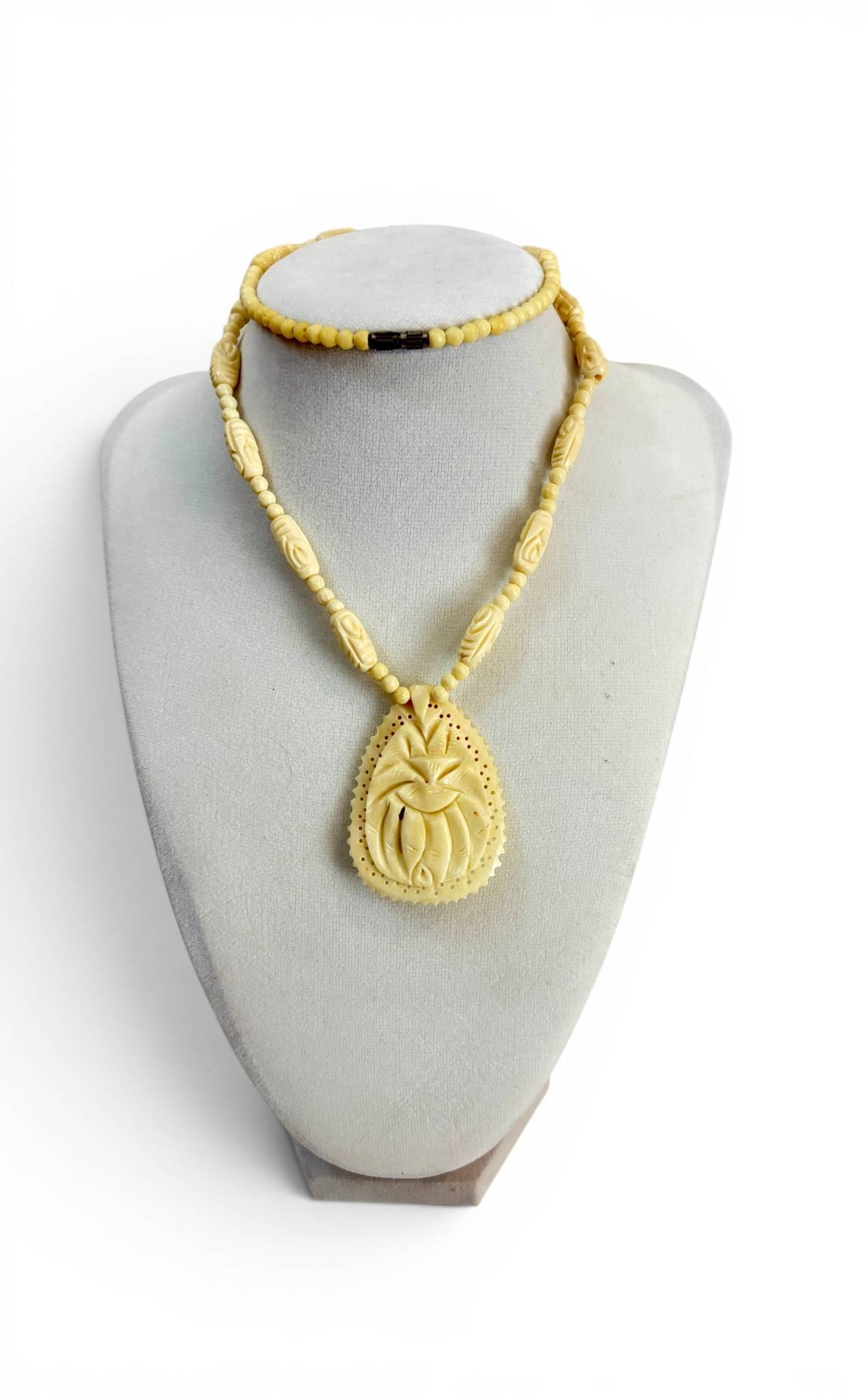 Carved Bone Necklace with Intricate Pendant: Carved bone necklace featuring a teardrop-shaped pendant with detailed patterns and perforations on the outer edge. The necklace includes larger carved oval beads interspersed with smaller round beads