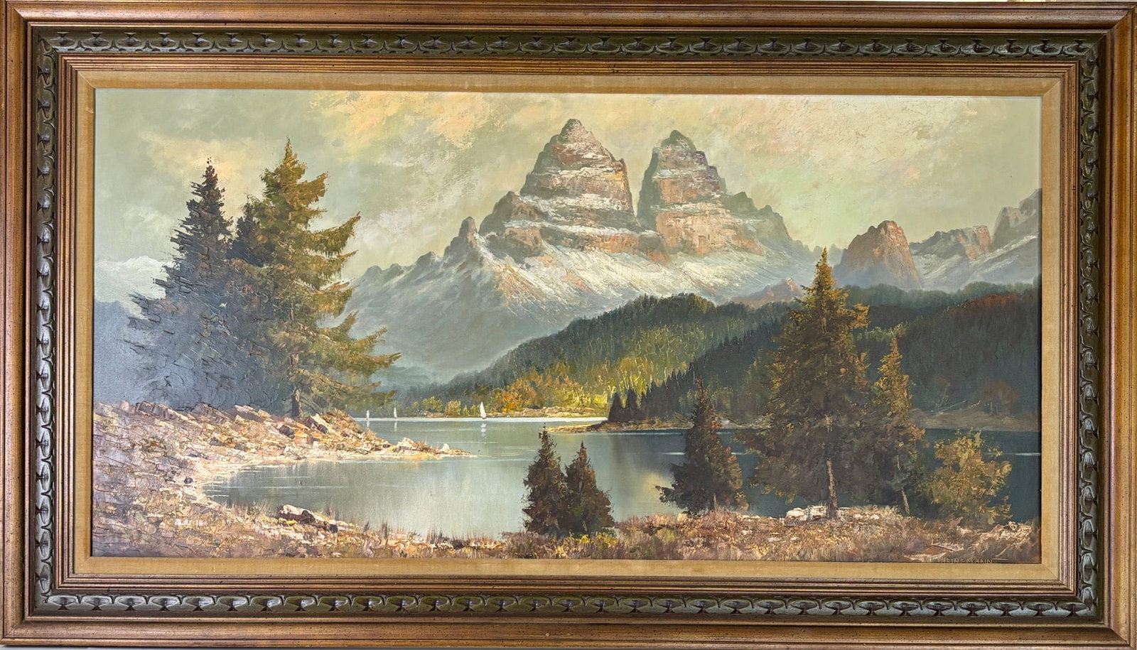 Mountain Landscape Oil on Canvas, Heinemann: Oil painting depicting a serene mountain and lake landscape with trees in the foreground under a soft, luminous sky. Signed ‘Heinemann’ in the lower corner. Displayed in a carved, gilt-finish wood