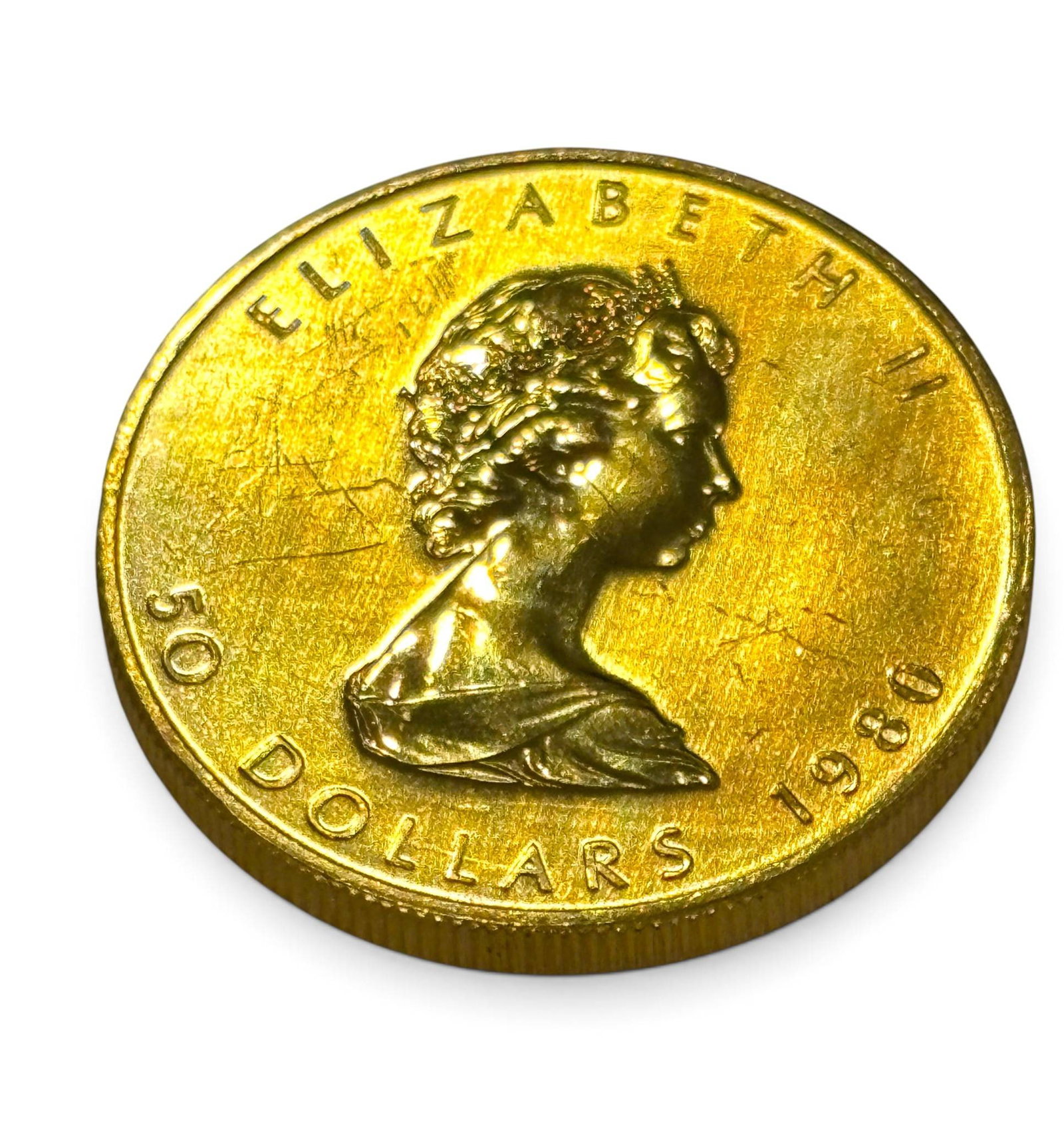 1980 Canadian 50 Gold Maple Leaf Coin: A 1980 Canadian 50 dollar Maple Leaf bullion coin made from 1 ounce of .999 fine gold. The obverse features Queen Elizabeth II, while the reverse displays a detailed maple leaf design. “Elizabeth II
