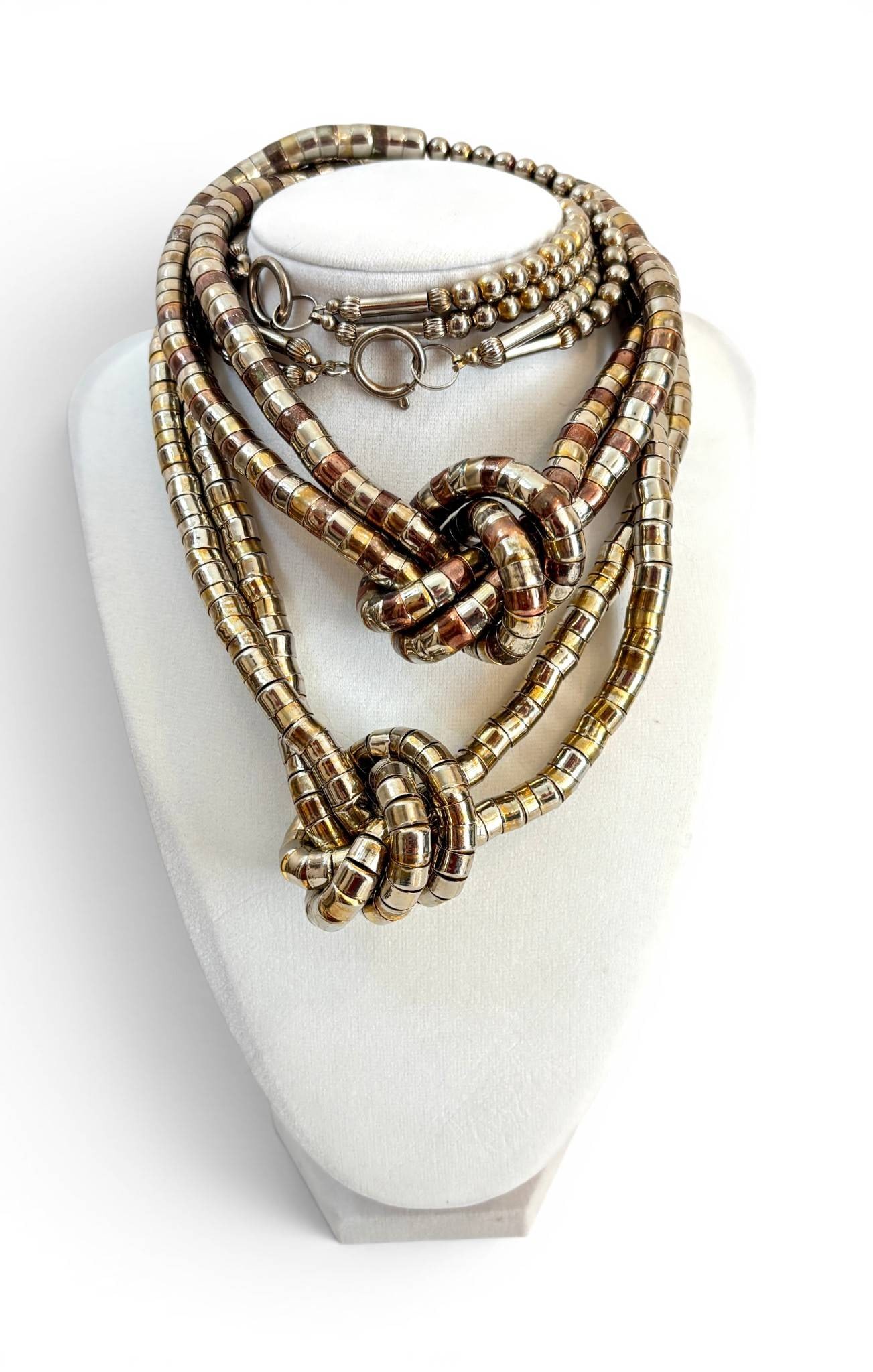 Multi-Strand Mixed Metal Knotted Necklaces: Necklace featuring multi-strand cylindrical and spherical beads in a mix of gold-tone, silver-tone, and copper-tone metals. The central design forms a decorative knot, showcasing the interwoven strand