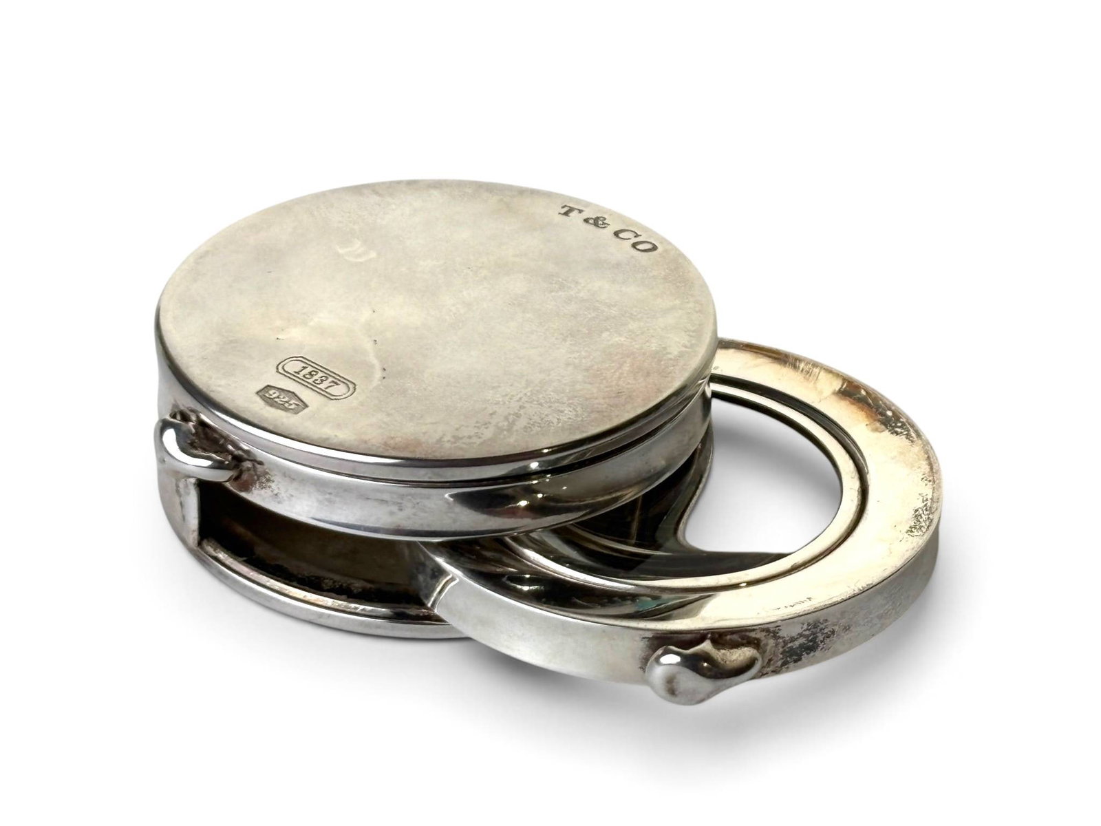 Tiffany and Co. Sterling Silver Folding Magnifying Glass: A circular sterling silver folding magnifying glass by Tiffany and Co., crafted in 2000. Markings include ‘T&Co,’ ‘1837,’ and ‘925.’ Features a hinged mechanism that conceals the glass