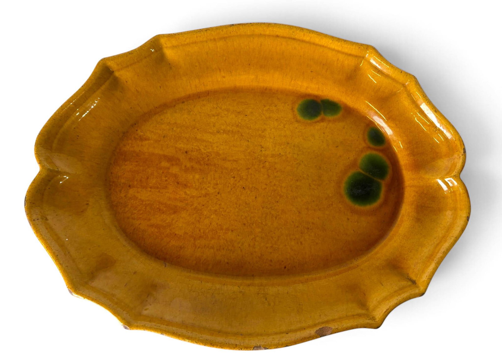 French Biot Glazed Terracotta Platter with Scalloped Edge: Glazed terracotta platter attributed to Biot with a fine ochre glaze and green accents. Features a scalloped edge and a stamped maker’s mark on the underside. Visible craquelure, glaze imperfections