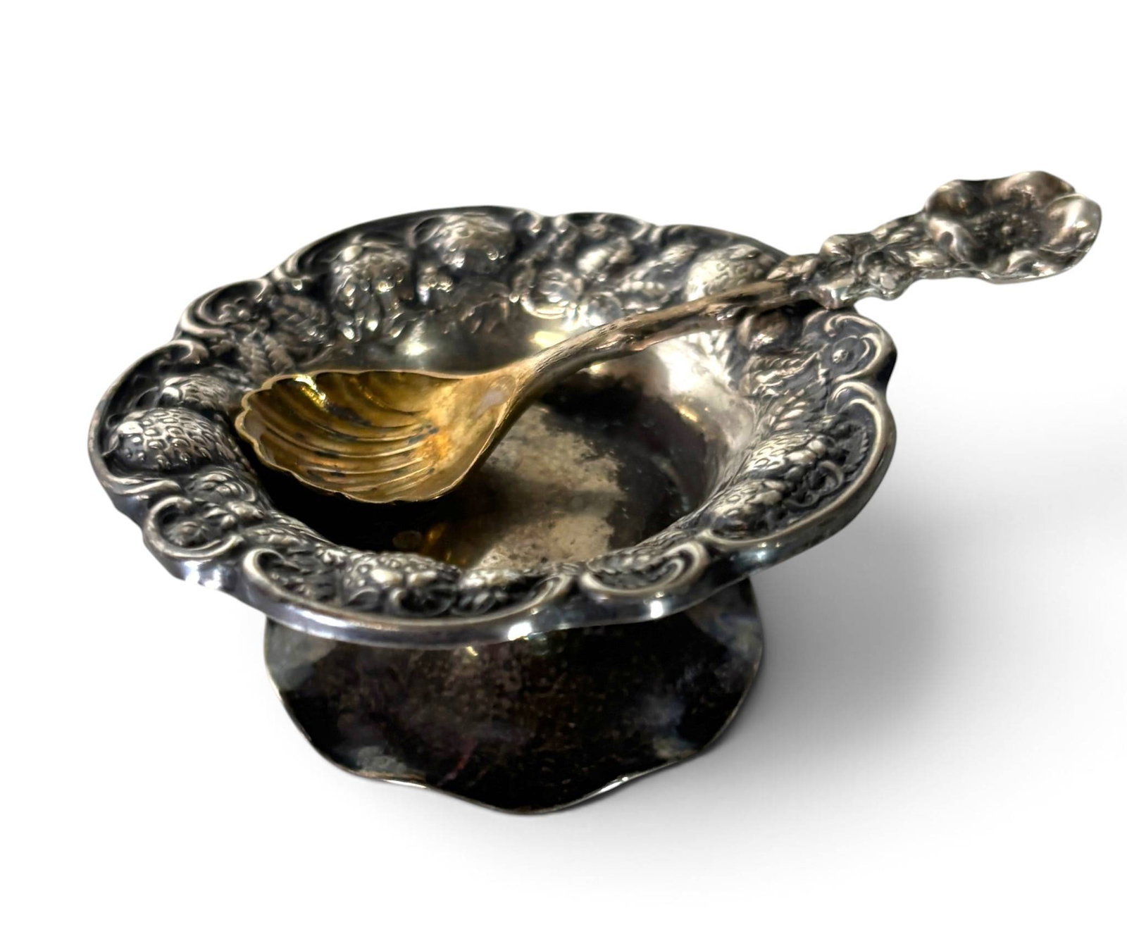Sterling Silver Salt Dish with Molded Floral Spoon: Sterling silver pedestal salt dish featuring an ornate scalloped rim and raised floral motifs. Accompanied by a coordinating sterling silver spoon with a gold-washed, shell-shaped bowl and floral