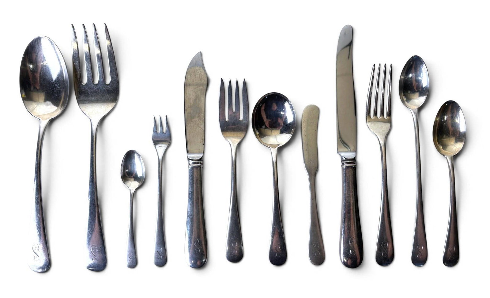 Monogramed Sterling Silver Flatware Set: Sterling silver flatware set by Coleman E. Adler and Sons, featuring a variety of utensils, including forks, knives, and spoons in multiple sizes. Pieces are monogrammed with the letter ‘S.’ Marki