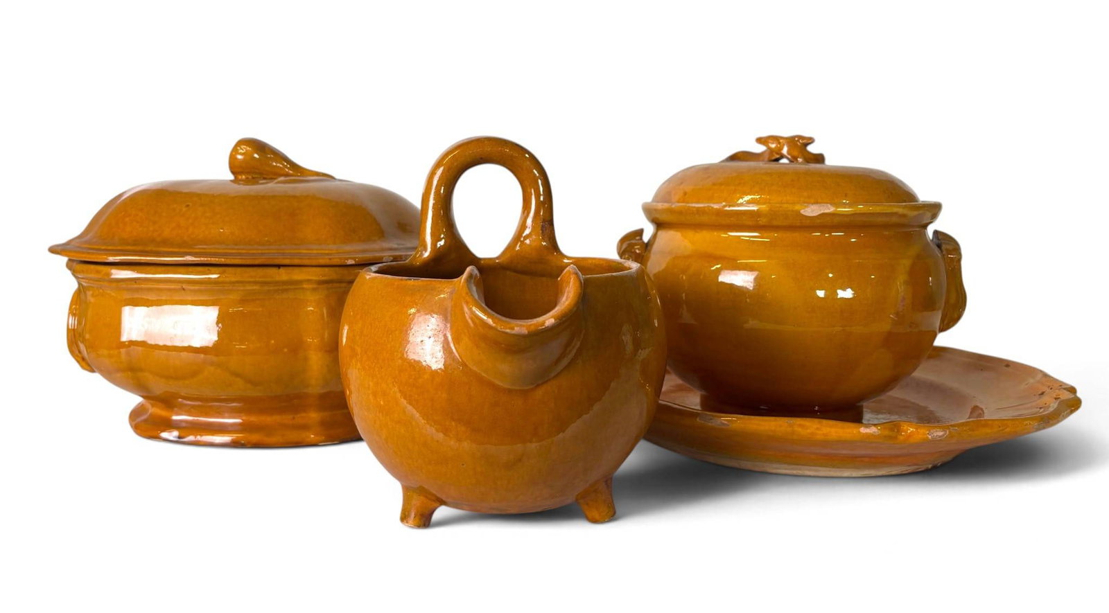 French Biot Glazed Terracotta Serving Pieces: Glazed earthenware serving pieces by Biot, France. Includes lidded tureens, a sauce boat with a handle, and a matching platter, all finished in a warm amber glaze. The collection features relief detai