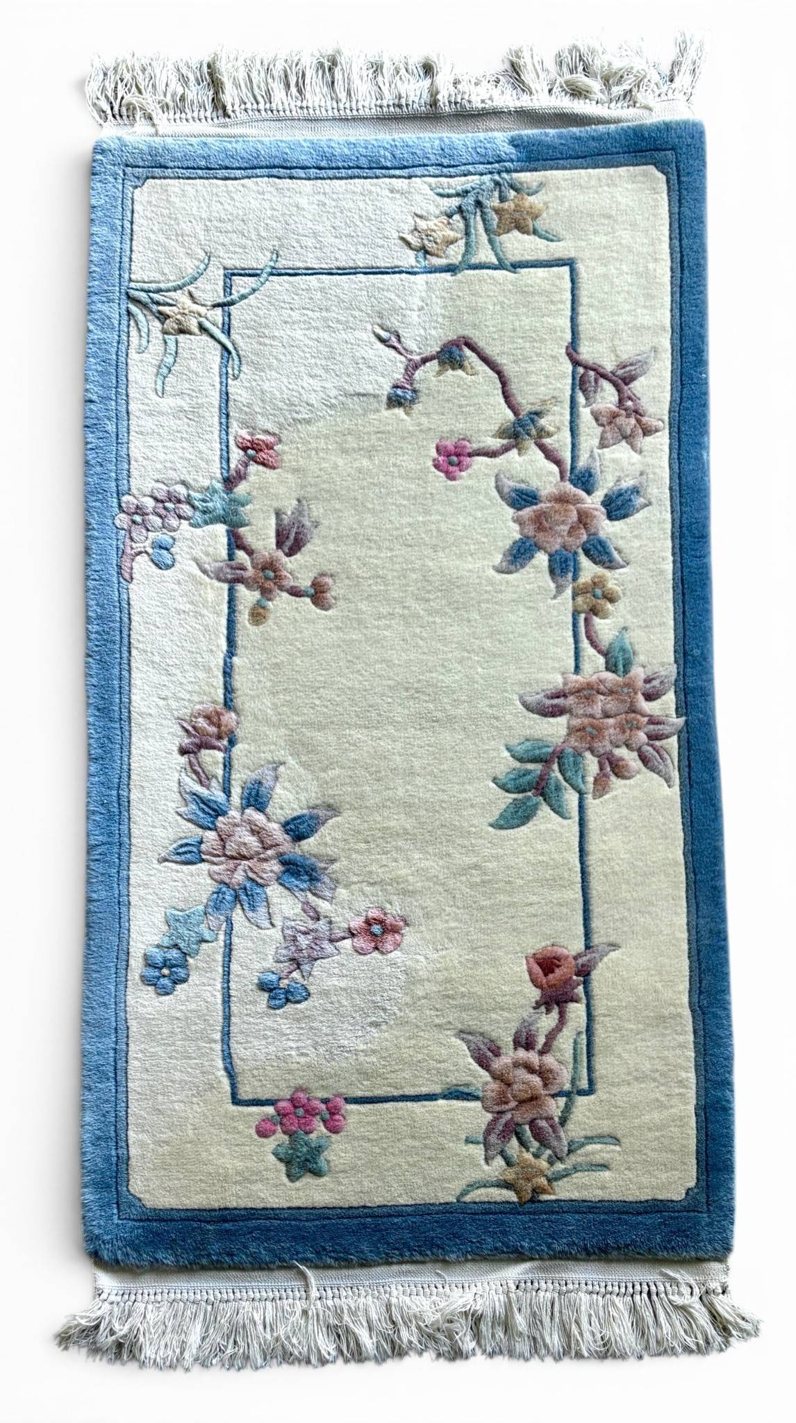 Handwoven Chinese Art Deco Revival Wool Rug: Handwoven Chinese Art Deco Revival rug crafted from wool. Features a cream field bordered by light and dark blue tones, adorned with stylized floral motifs in pastel shades. The rug includes fringe