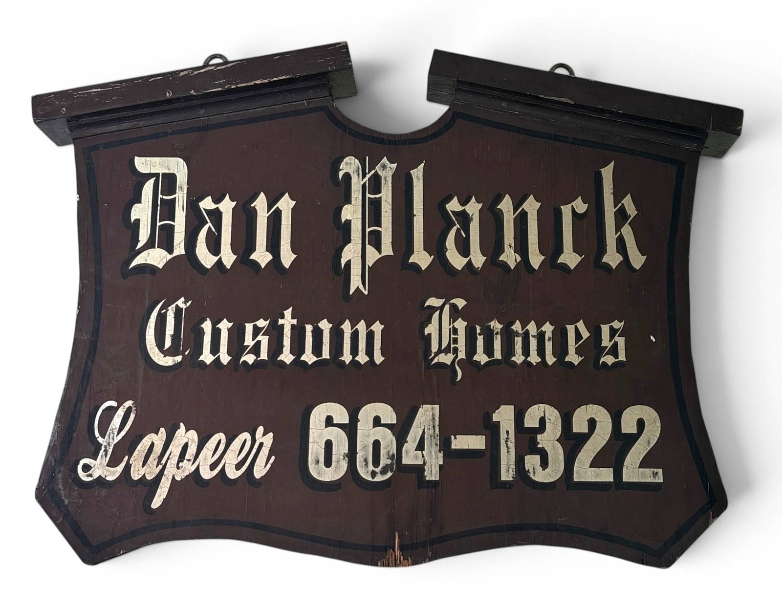 Antique Wooden Advertising Sign Lapeer Michigan: Hand-painted wooden advertising sign featuring text in a decorative white serif font against a dark brown background. The sign advertises ‘Dan Planck Custom Homes’ with a phone number and