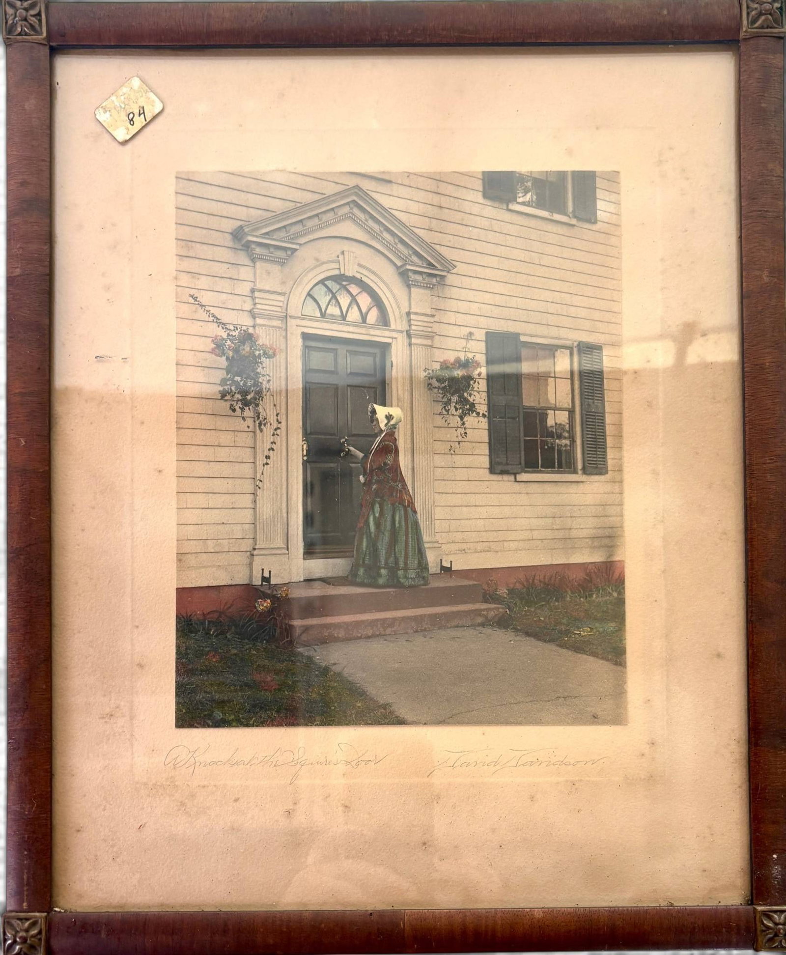 A Knock at the Parson’s Door’ by David Davidson: Hand-colored photo titled ‘A Knock at the Parson’s Door,’ attributed to David Davidson, as signed on the mat. Depicts a woman in period attire knocking on a detailed wooden door. Set in a