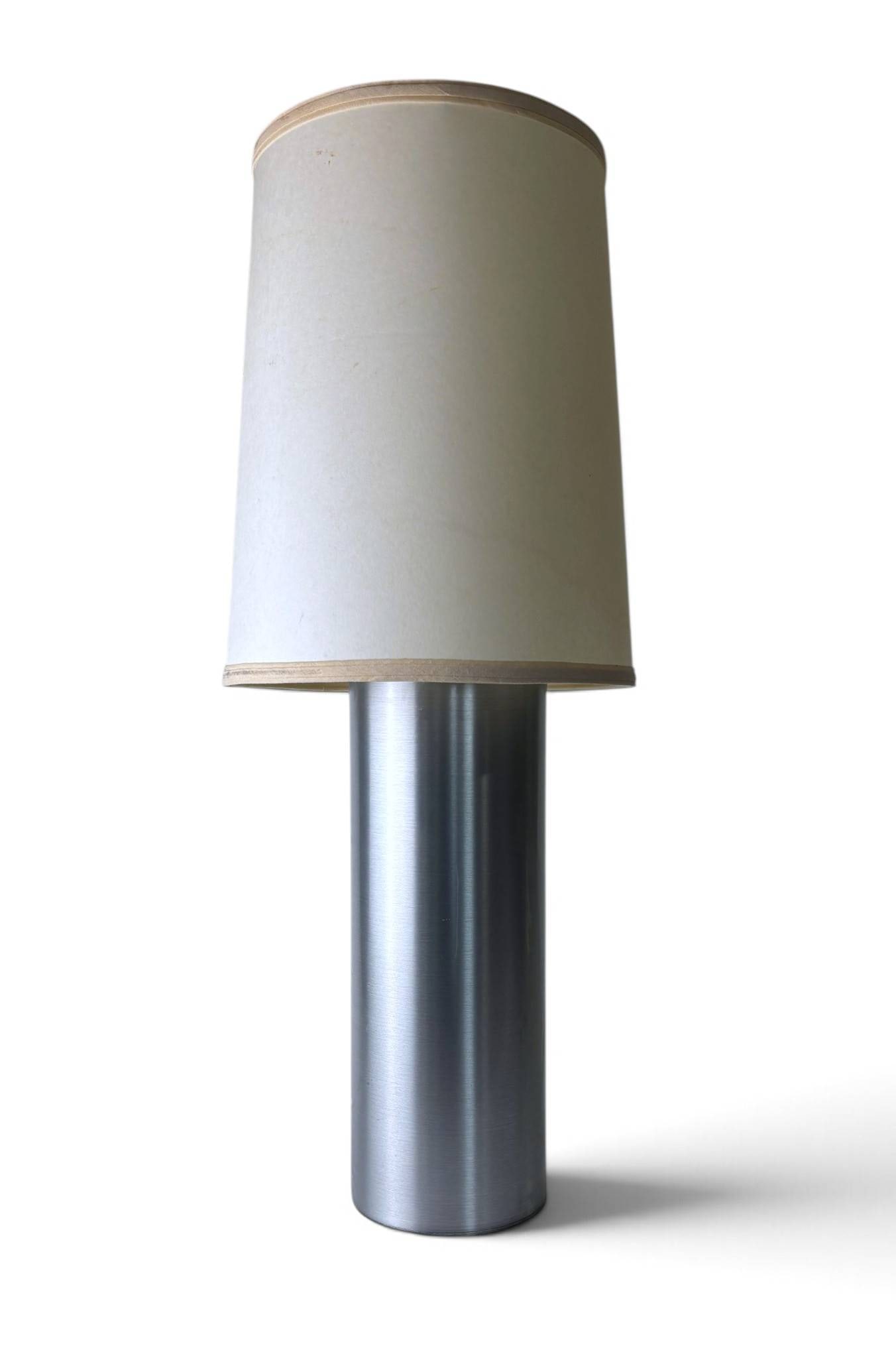 Mid-Century Modern Aluminum Table Lamp: Mid-Century Modern table lamp featuring a brushed aluminum cylindrical base with a silver finish. Includes a metal harp and socket assembly and a cream-colored shade with wood trim accents. The lamp b