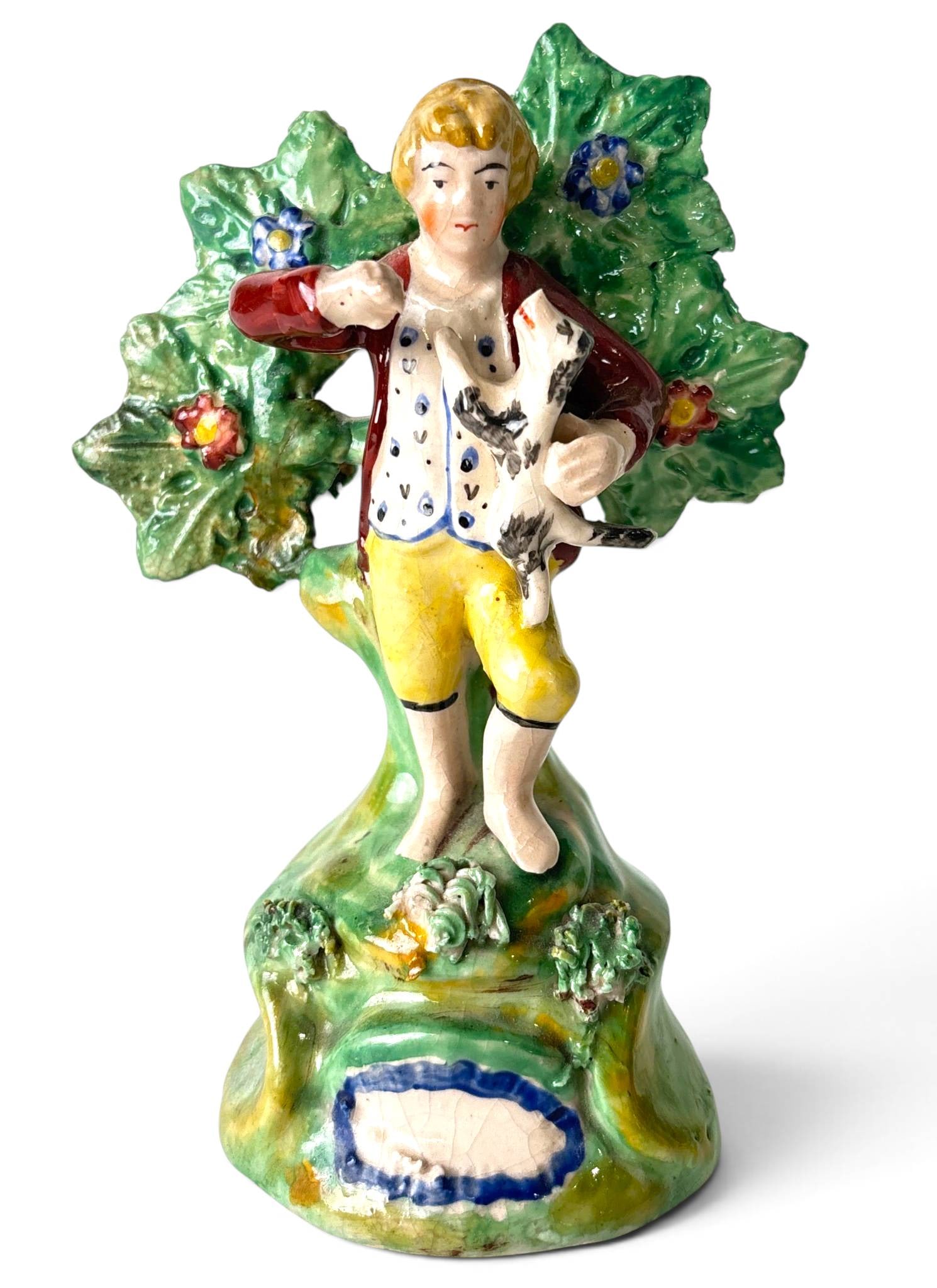 Antique Staffordshire Porcelain Pearlware Bocage Figure: Staffordshire porcelain pearlware bocage figure depicting a boy in yellow breeches and red coat holding a small dog, set against a tree with detailed floral bocage decoration. The vibrant polychrome g