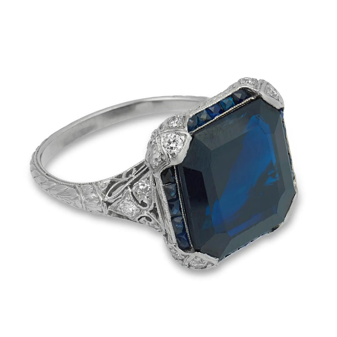 ART DECO STYLE SAPPHIRE AND DIAMOND RING, WHITE GOLD / PLATINUM: ART DECO STYLE SAPPHIRE AND DIAMOND RING, WHITE GOLD / PLATINUM Description: The ring is centered on a substantial rectangular step-cut sapphire, exhibiting a deep, saturated blue tone with strong geo