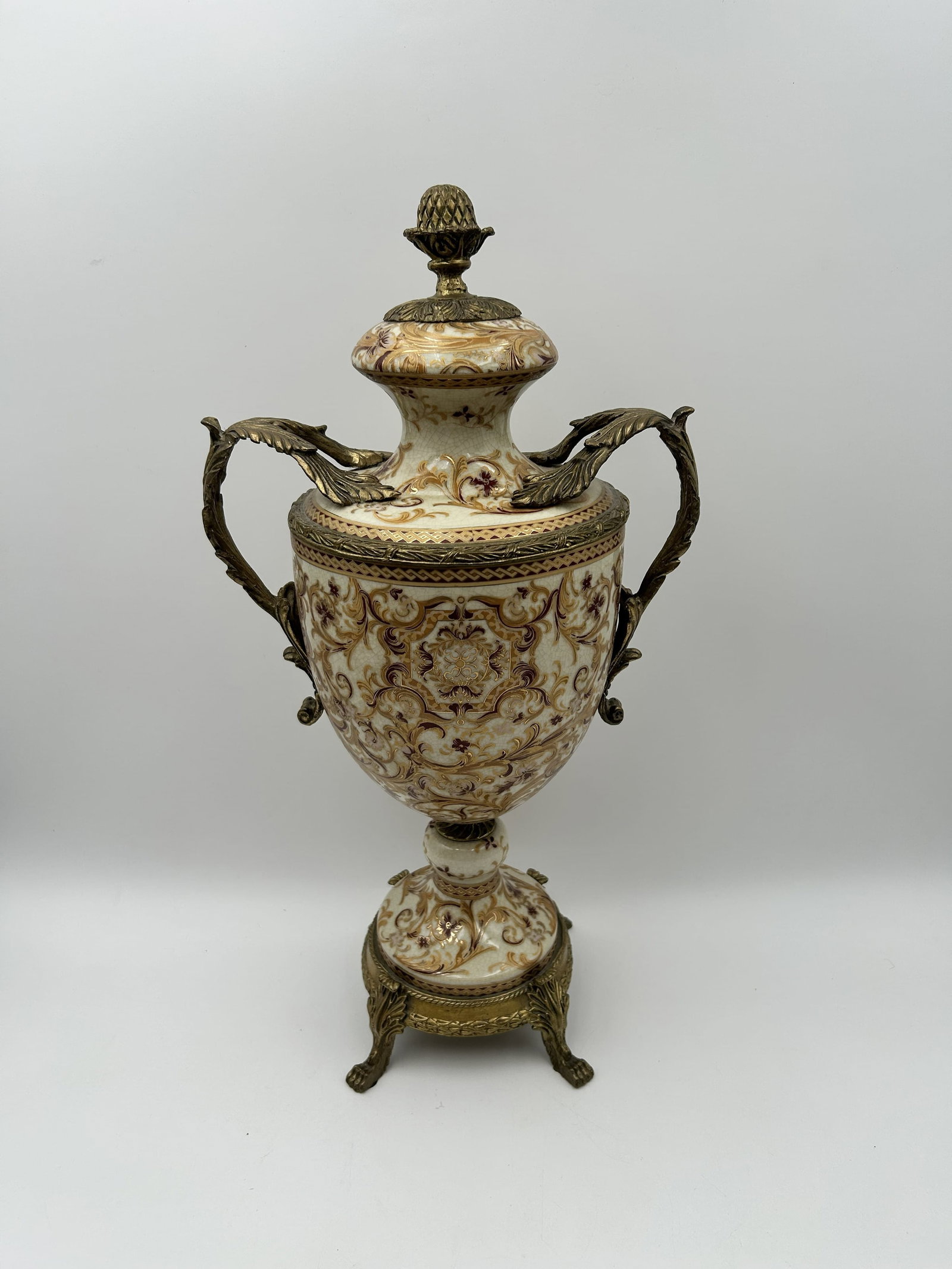 Ornate Porcelain and Bronze Urn: This is an ornate urn featuring intricate hand-painted porcelain decorated with gold, brown, and floral patterns, accented with gilt bronze mounts, handles and a base. Dimensions: - 11" W (at handles)