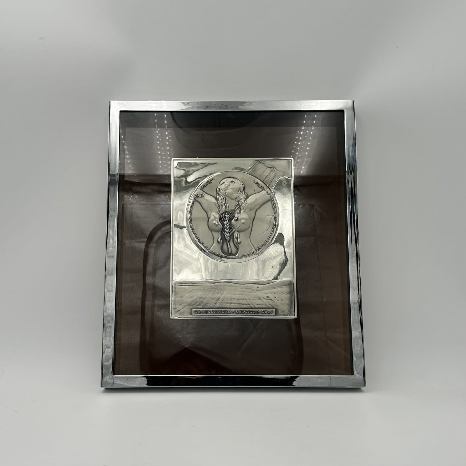 Salvador Dali "La Fecundidad" Sterling Silver Relief Plaque mounted in Chrome Shadowbox Frame: This is a Salvador Dali "La Fecundidad" sterling silver relief plaque mounted in a chrome shadowbox frame, Limited Edition. Dimensions: - Framed - 13" W x 15" H - Unframed - 6.5" W x 8.5" H