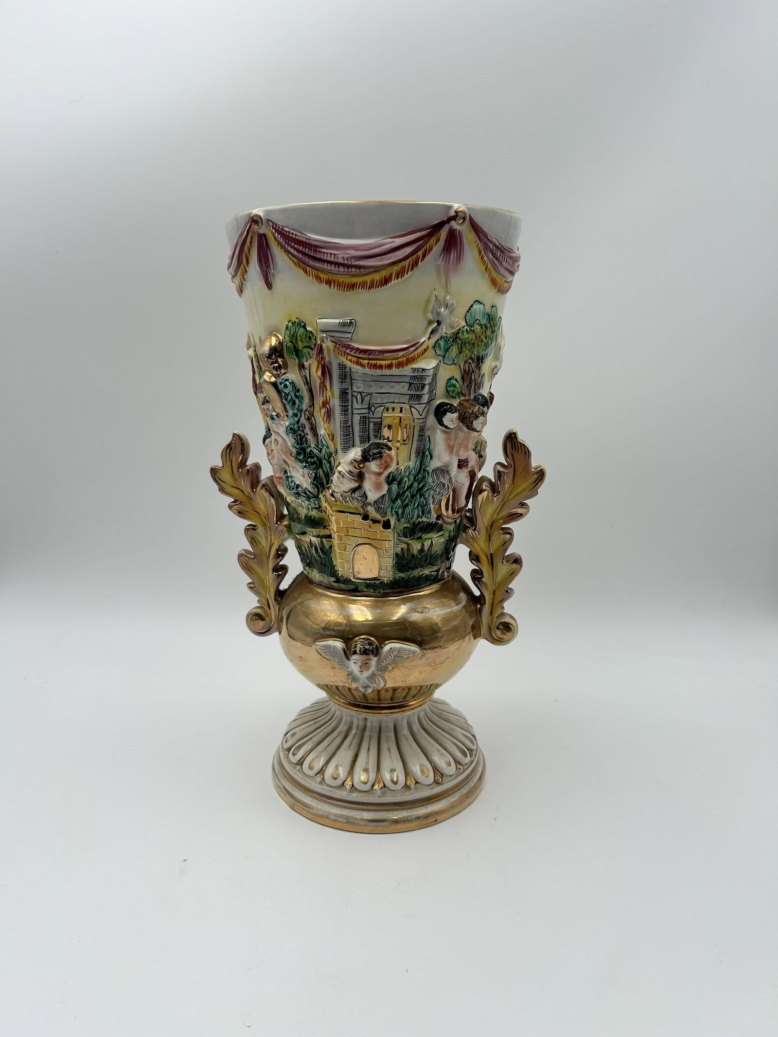 Vintage Capodimonte Porcelain Vase featuring embossed Cherubs: This is a vintage Italian Capodimonte porcelain vase featuring embossed cherubs and gold gilded accents. The vase is crafted in a relief design depicting scenes of cherubs or putti in a garden setting