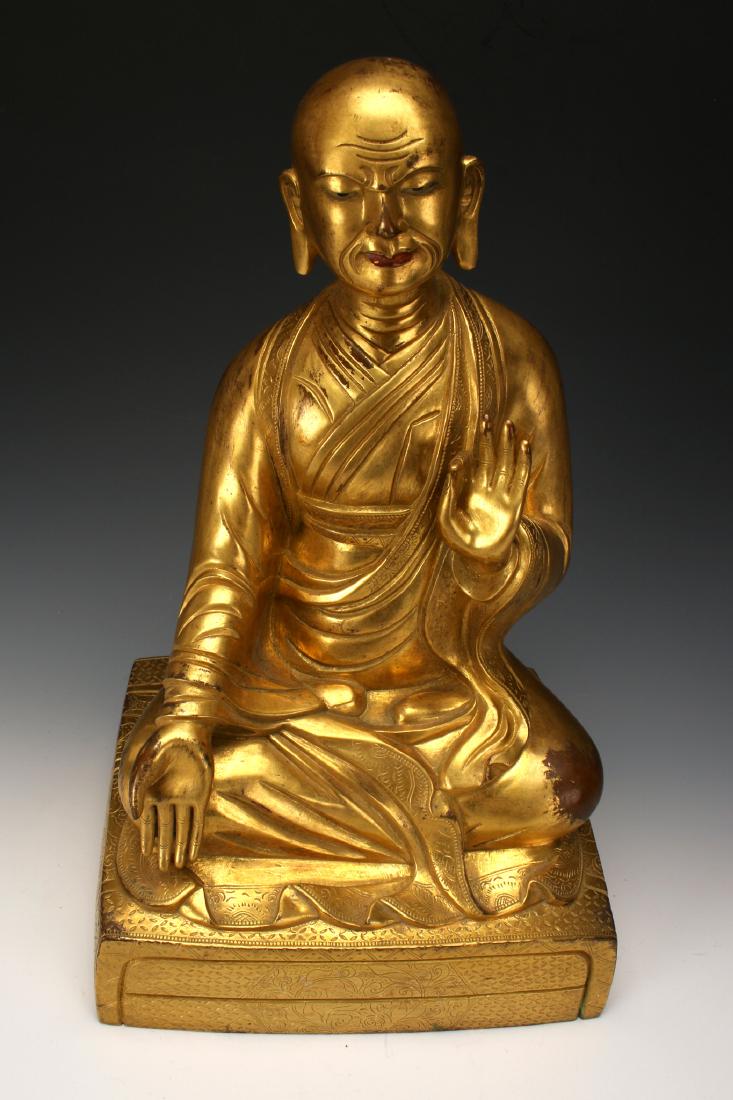 BRONZE BUDDHA: Bronze Buddha: A bronze teaching Buddha in flowing robes, seating in the lotus position on top of a raised cushion. His earlobes are elongated, and has a contemplative expression. Marked on the botto