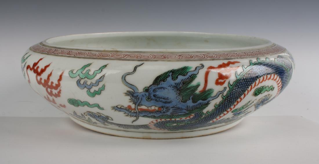 FAMILLE ROSE KANG XI DRAGON BOWL: Famille Rose Kang Xi Dragon Bowl: The center of this low bowl has a green dragon, with claws extended, flying among flaming clouds. The outside has a pair of dragons, green and blue, flying among fla