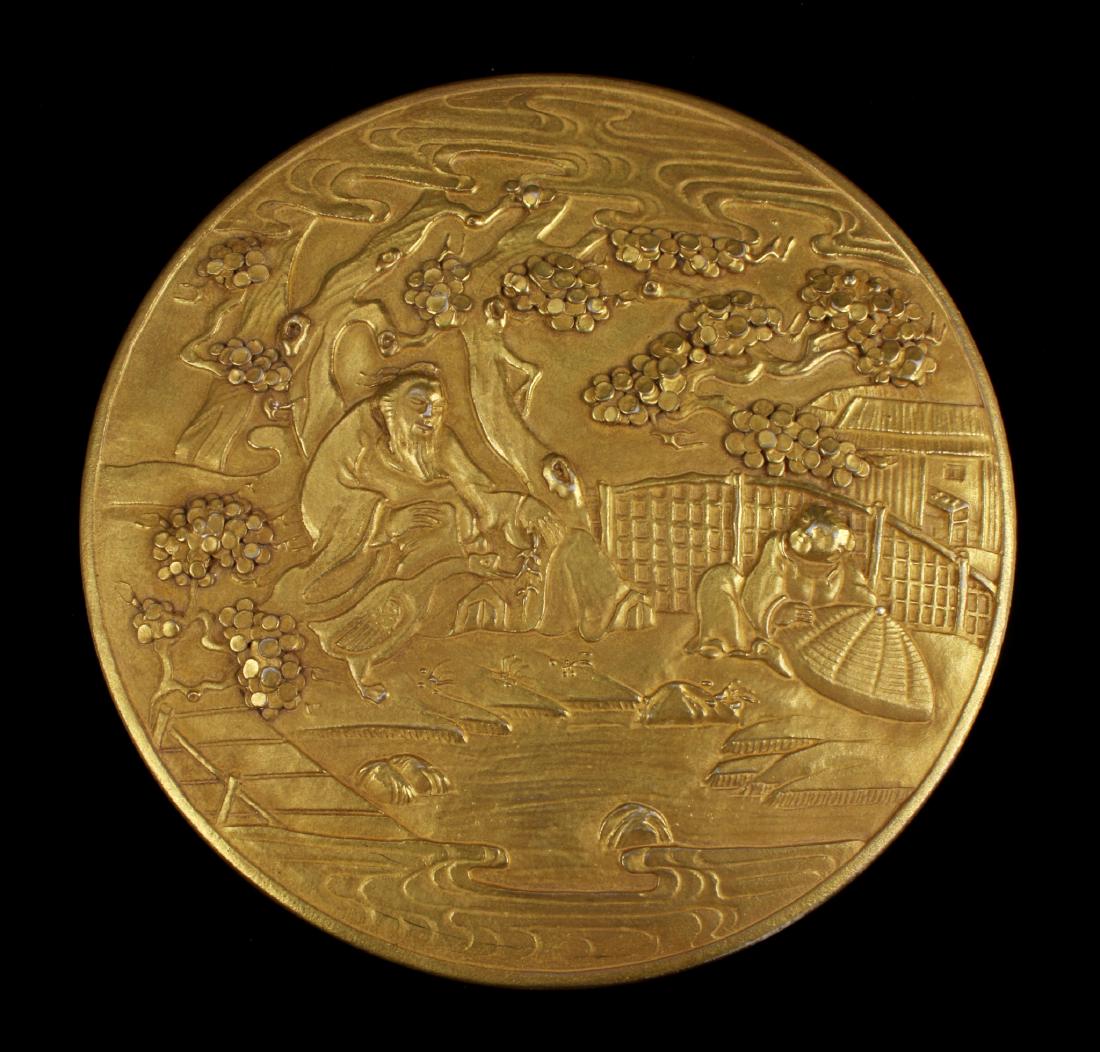 GOLD CERAMIC CIRCULAR BOX: Gold Ceramic Circular Box: This circular box has a village scene on the lid. An elder feeds a goose near a child, all under trees and by a stream. Clouds are overhead and there is a house in the back