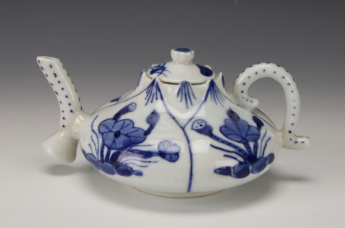 BLUE & WHITE LIDDED TEA POT: Blue & White Lidded Tea Pot: A small, delicate tea pot in the shape of a lotus bud. The petal peaks at the lid. Each petal shape contains a scene of lily pads. It has an applied curved handle and 