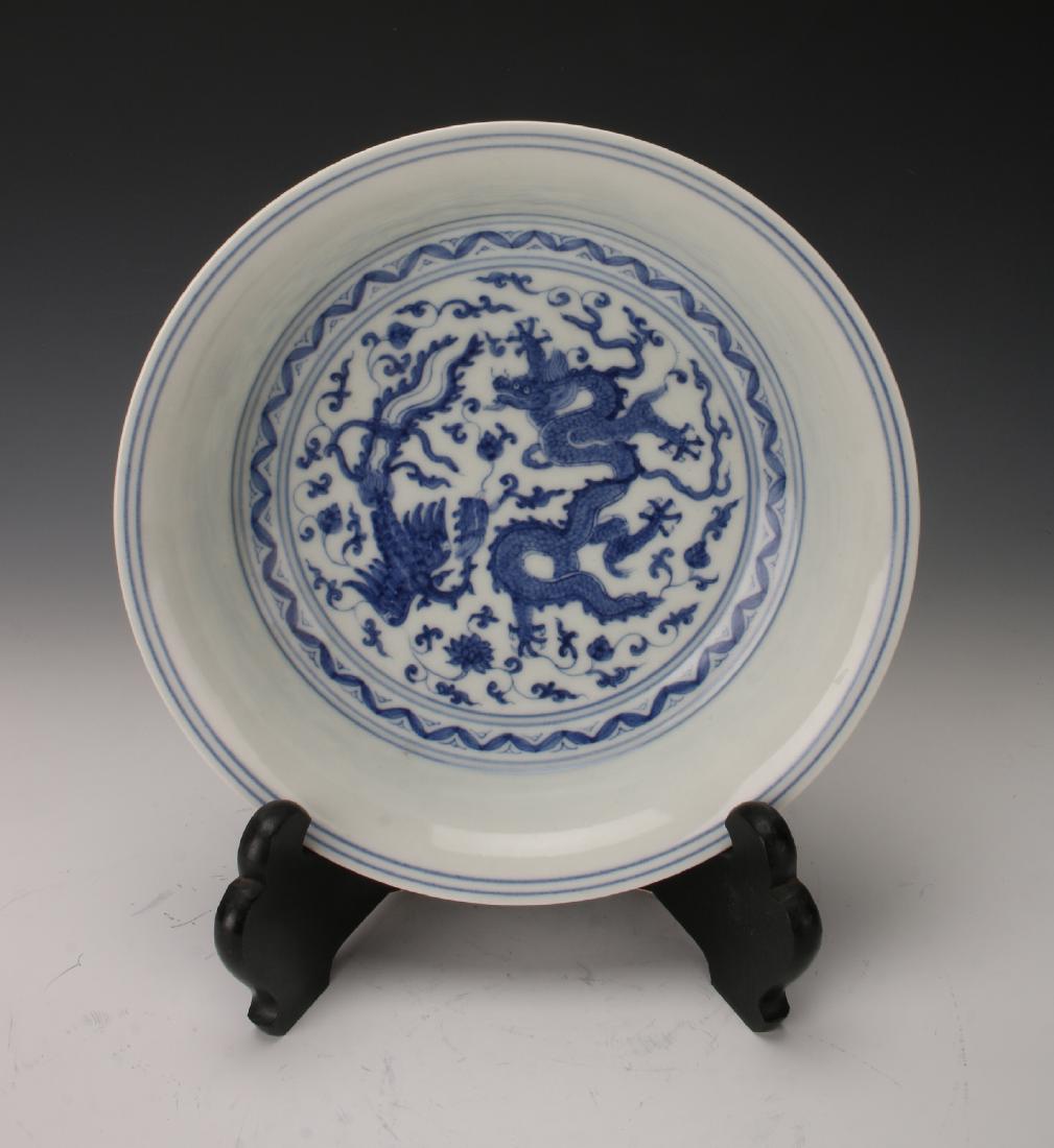 CHINESE BLUE & WHITE MING DYNASTY SAUCER: Chinese Blue & White Ming Dynasty Saucer: A saucer showing a central motif of a dragon and phoenix among vines, enclosed in a band of blue lines on the inside and at the rim. The outside rim conti