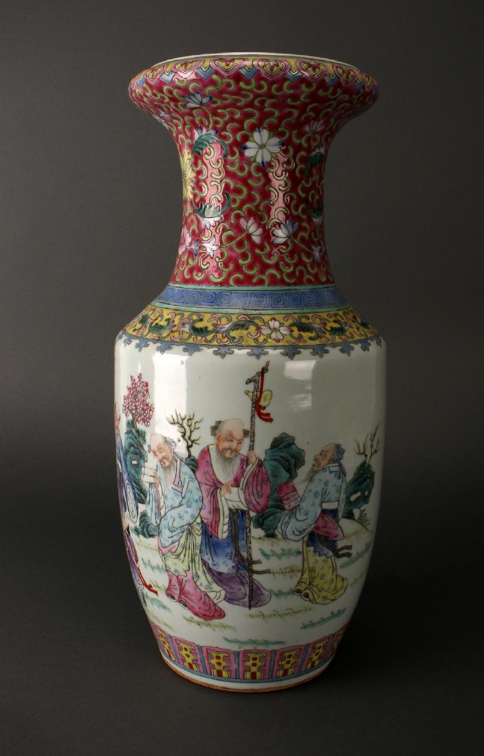 FAMILLE ROSE VASE: Famille Rose Vase: Elders in a garden adorn the body of this vase, they are observing a banner being held by two children. Bats fly near a boulder. The protruding lip has a ruyi border over a dark pin