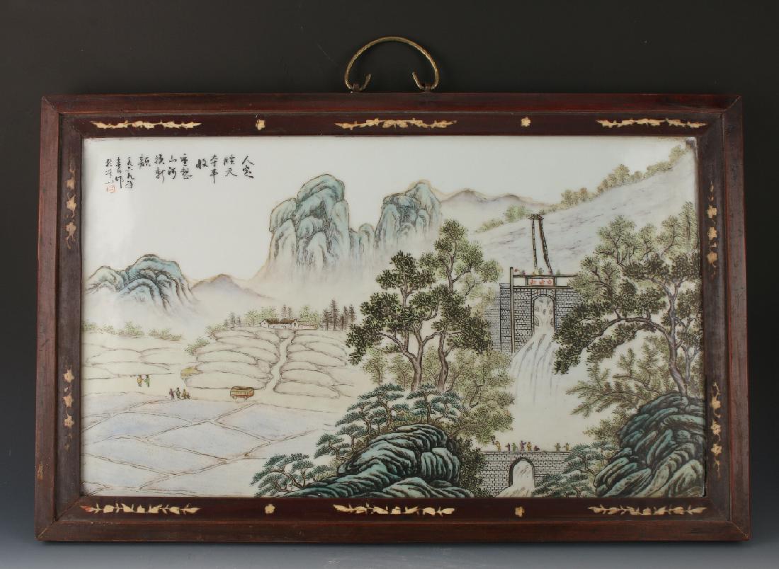 FRAMED PORCELAIN PLAQUE: Framed Porcelain Plaque: A mountain is in the background of this landscape scene with a waterfall and bridges to the right and a bus with people to the left. Calligraphy and artist mark on upper left.