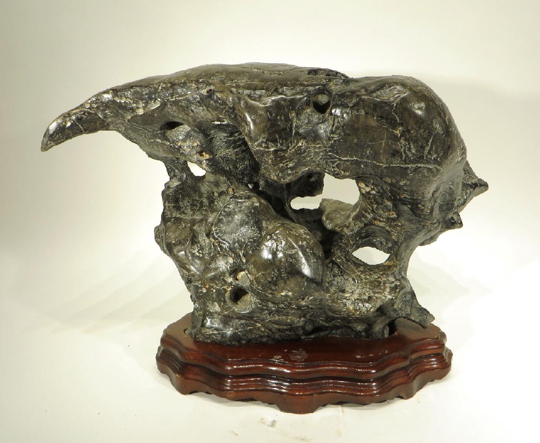 LING BI SCHOLAR'S STONE: Ling Bi Scholar's Stone : Gray scholar's stone pierced through in several places showing carving marks and some veining. Asymmetrical with a large overhanging side. Sits on a custom base.