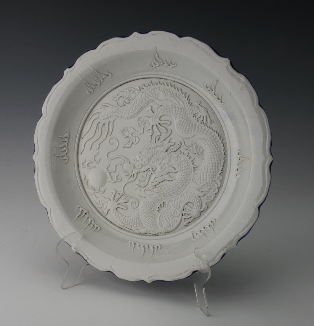 WANG BING RONG CARVED DRAGON PLATE: Wang Bing Rong Carved Dragon Plate: A dragon and a flaming pearl are carved in bas relief in the center of the dish. The border has flames. The bottom rim is glazed in cobalt blue. Marked on the botto