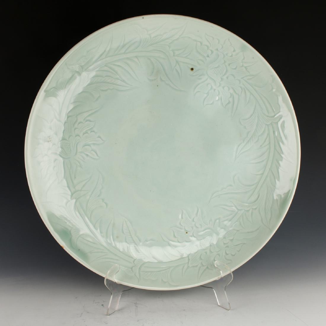 PALE CELADON CHARGER: Pale Celadon Charger: Incised decoration of peonies form a circular border. The decoration is accented by the glaze pooling in the depressions. Several iron spots dot the interior and exterior. Areas